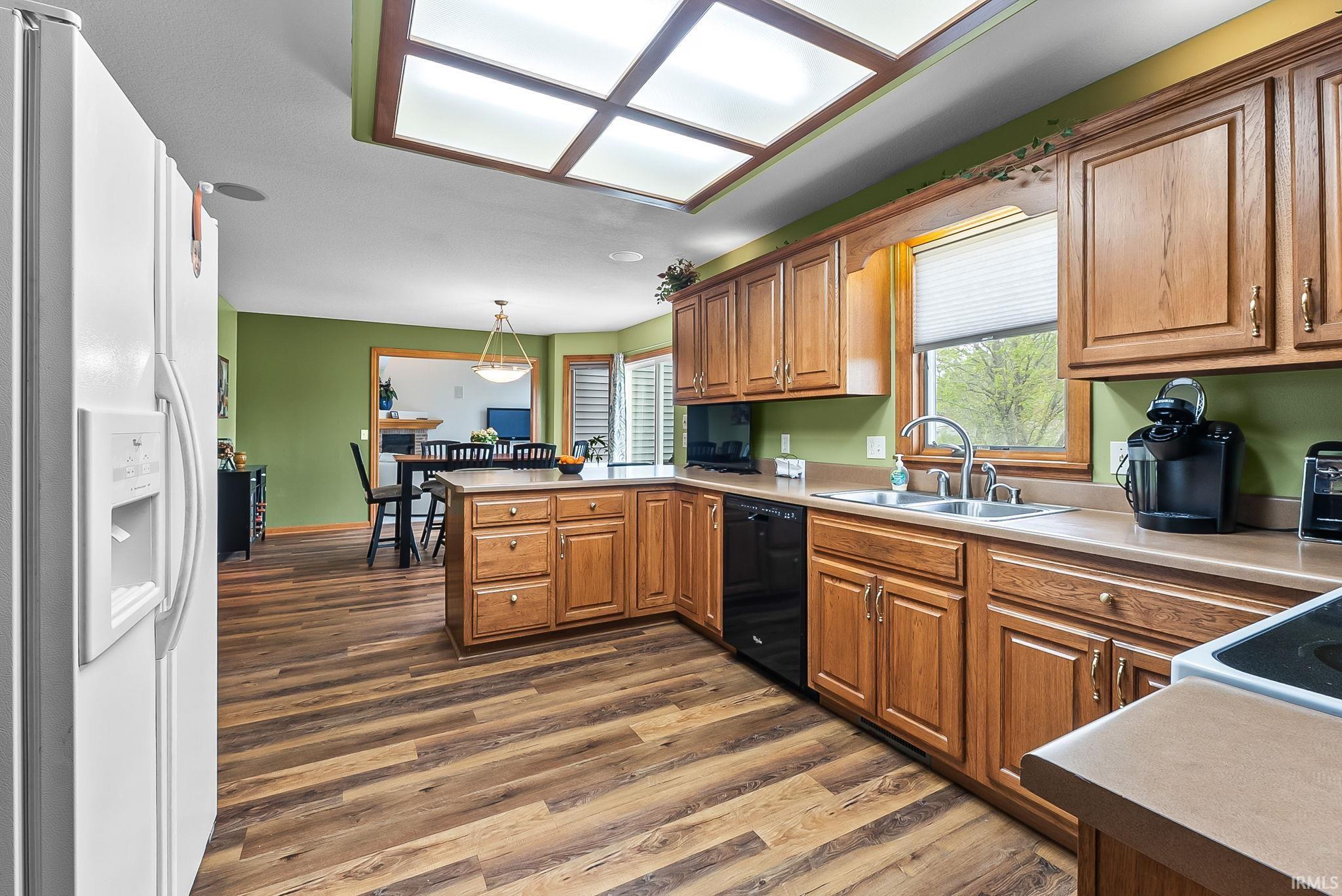 Kitchen featuring wood-finish flooring, a central island with countertop seating, wood cabinetry, a dual basin stainless steel sink, and a multi-panel ceiling light fixture
