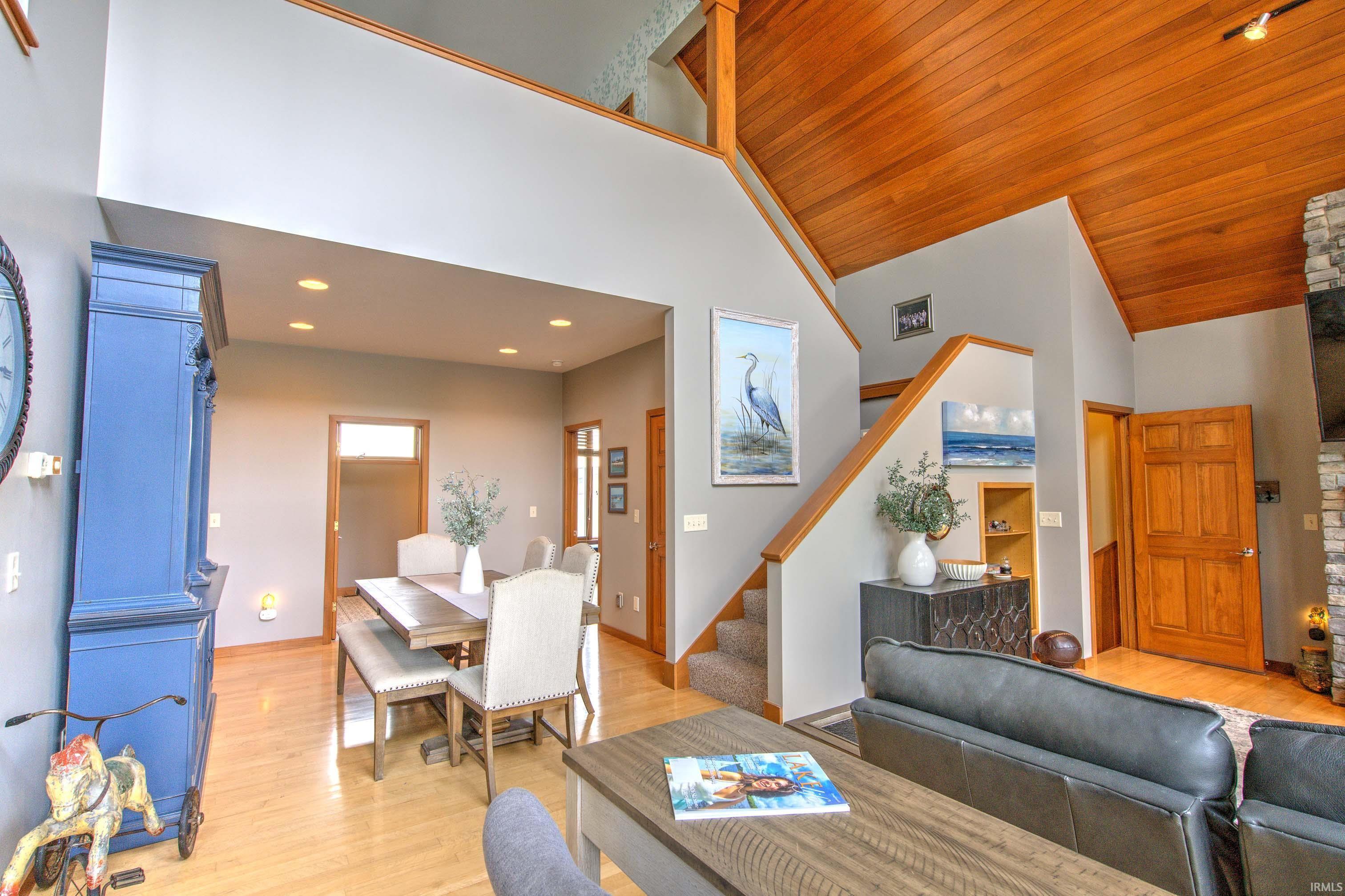 Two-story living area featuring a vaulted wood-paneled ceiling, light wood-finish flooring, a carpeted staircase with wood railing, and recessed lighting