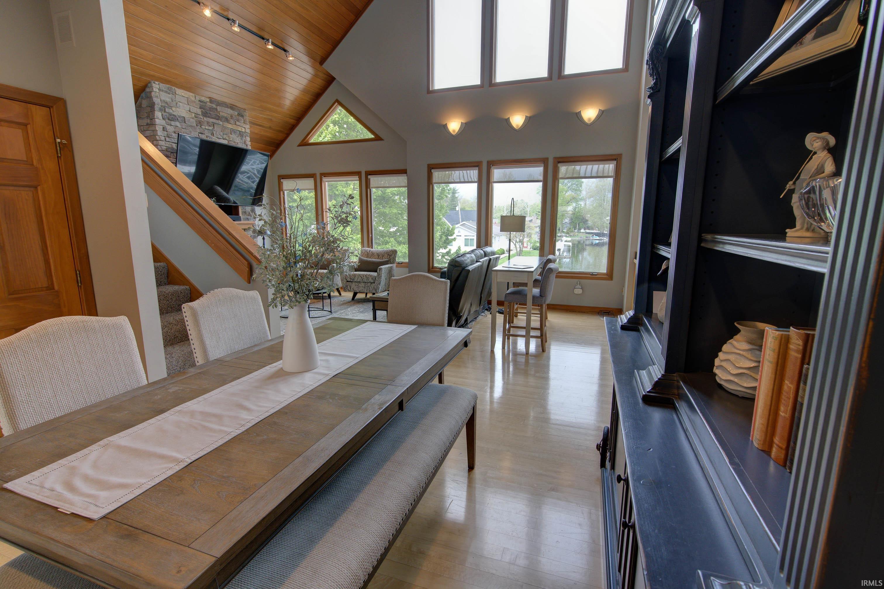Open-concept living space featuring a vaulted wood-paneled ceiling, a stone-clad fireplace, and expansive windows