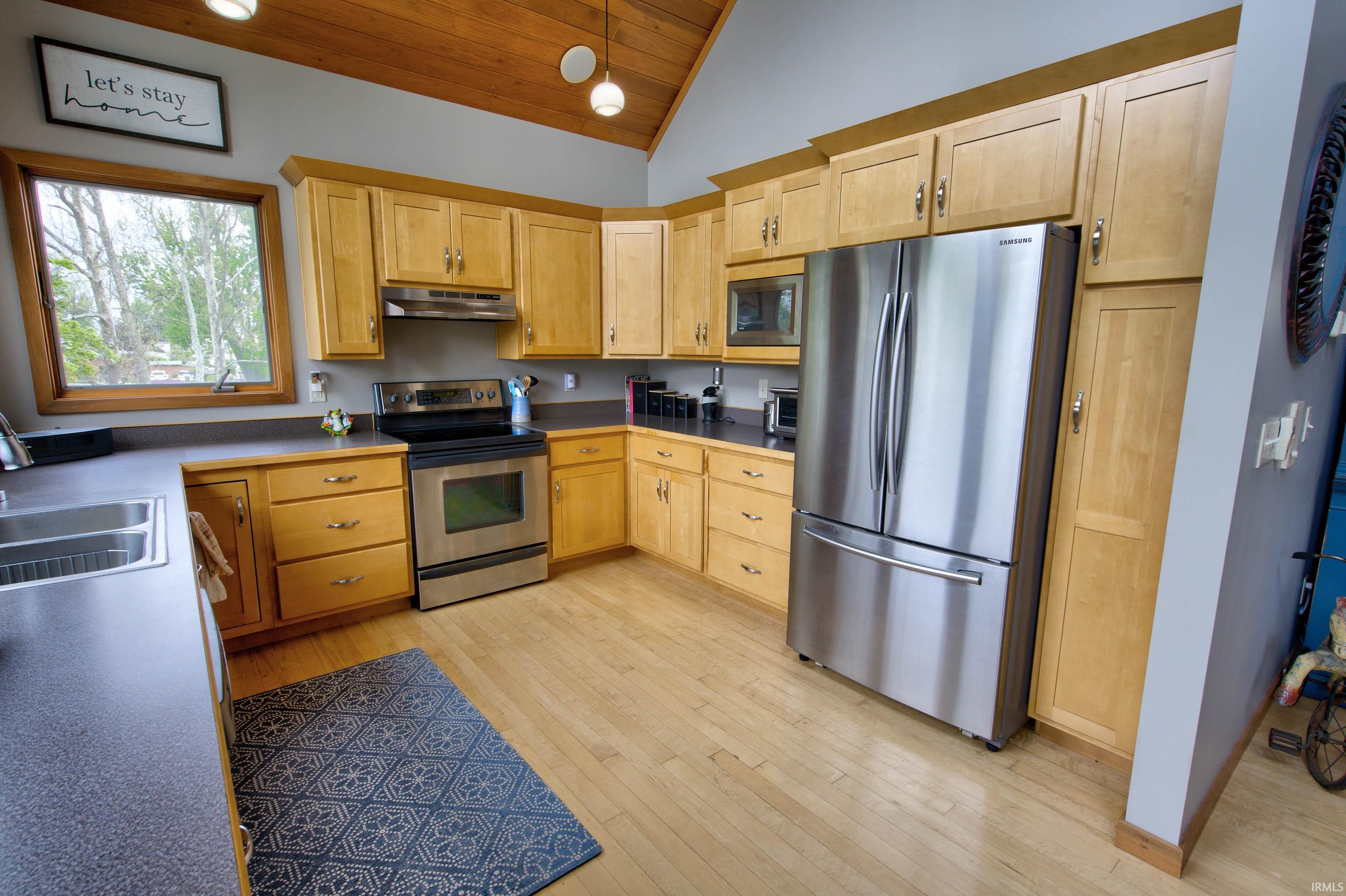 Kitchen featuring natural wood cabinetry, stainless steel appliances, dark countertops, and wood-finish flooring