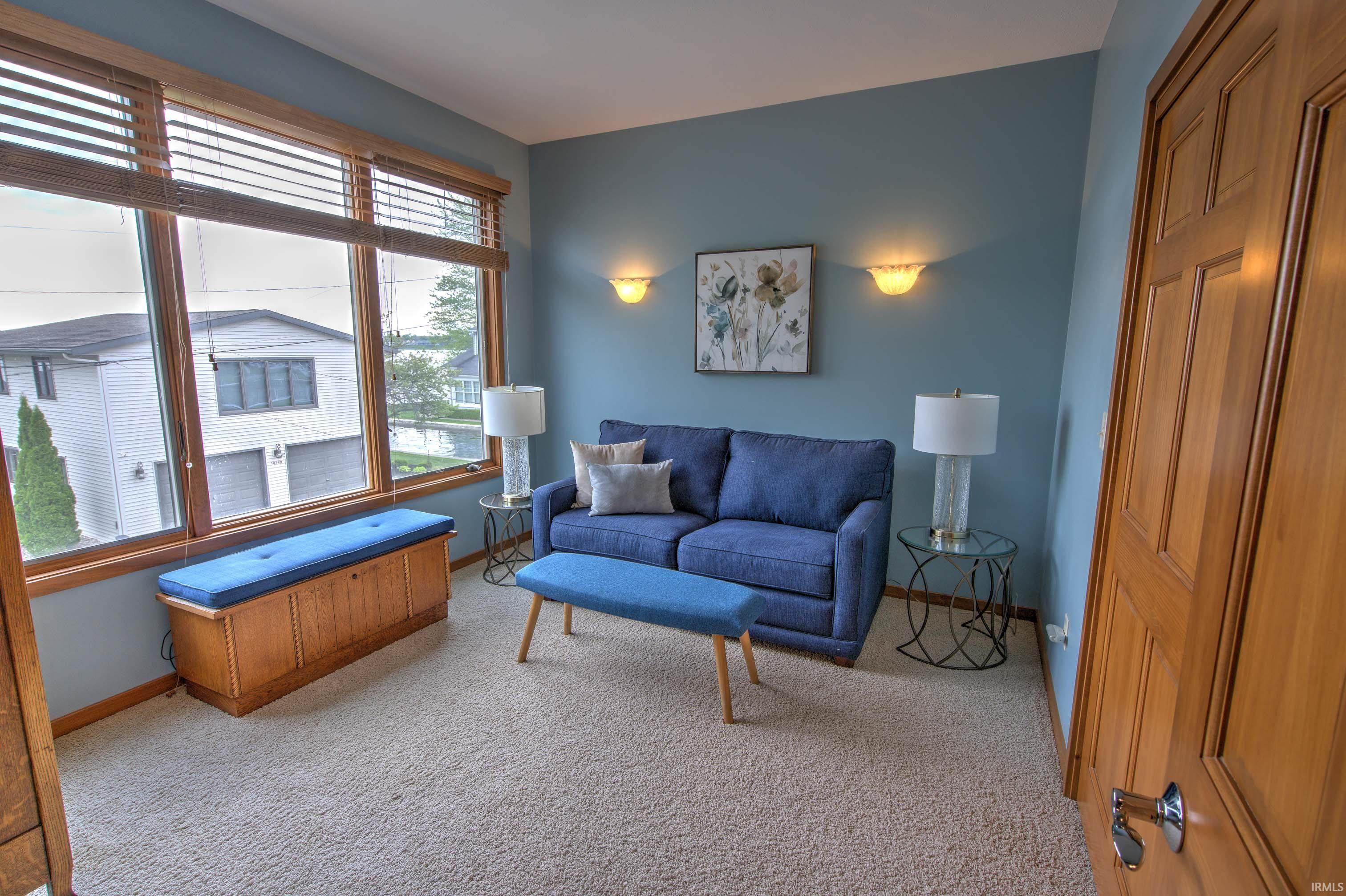 Carpeted room featuring a large window with wooden blinds, a built-in wooden storage bench, and sconce lighting