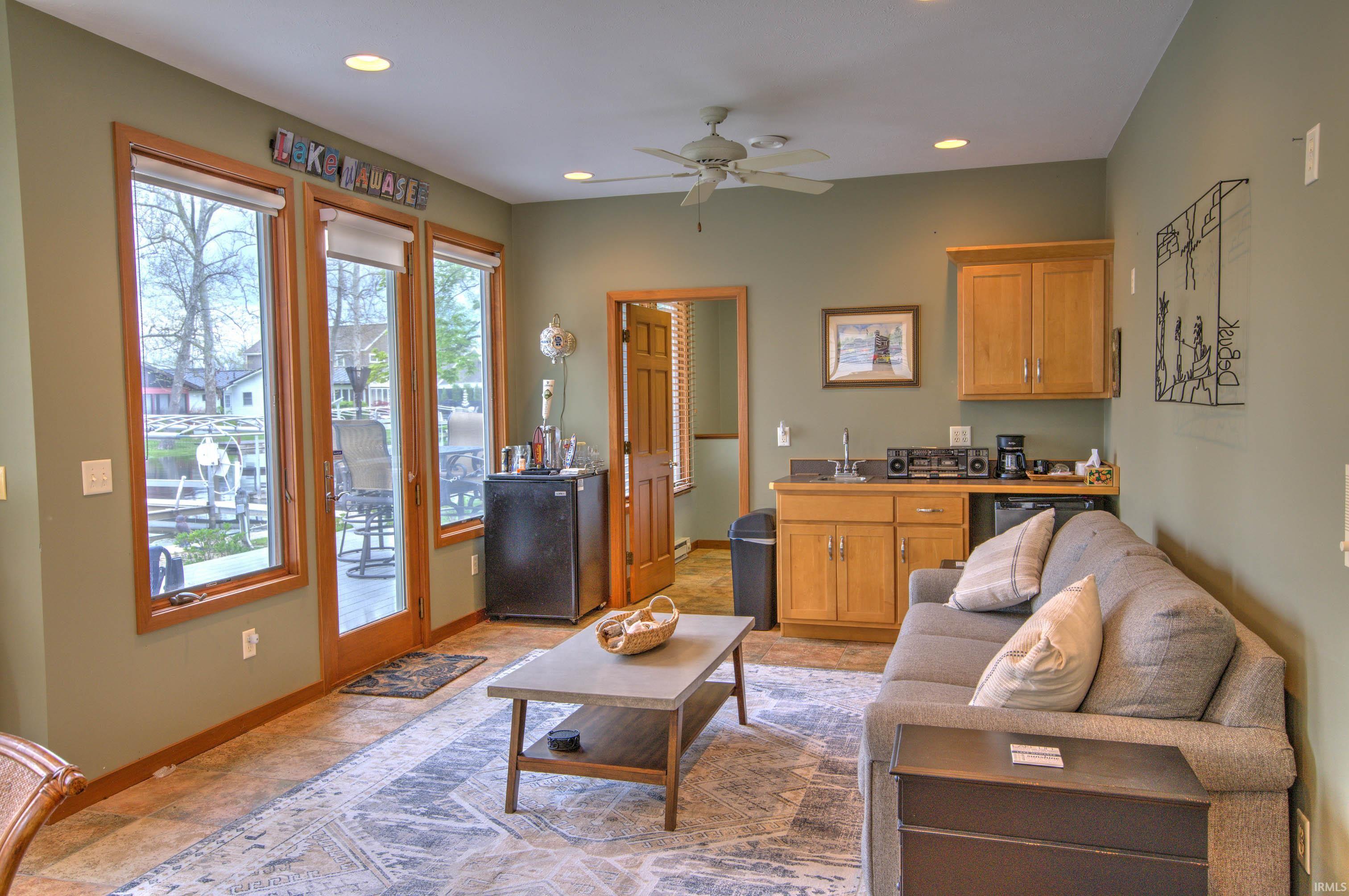 Entertainment space featuring three large glass panel doors, a built-in wet bar with wood cabinetry, recessed lighting, and a ceiling fan