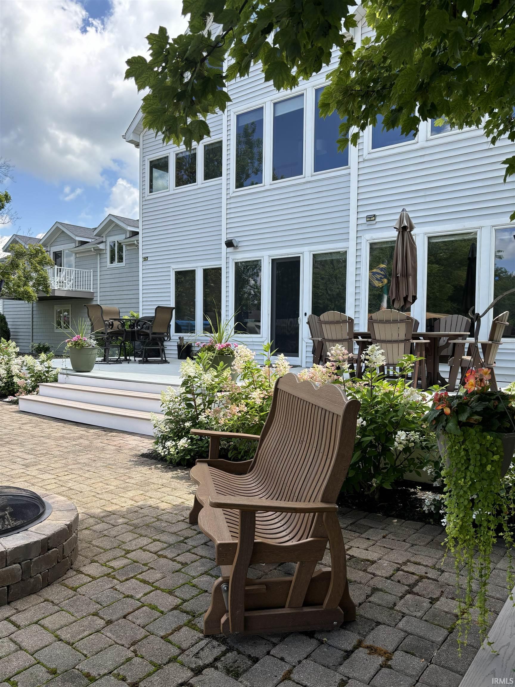Expansive paver patio featuring a stone fire pit, wood-finish bench, and a multi-level deck with white railings