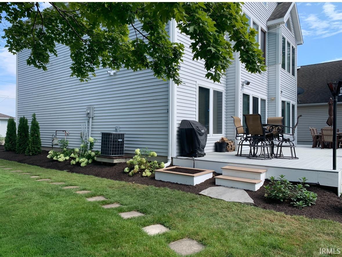 Expansive rear exterior featuring a multi-level composite deck, manicured lawn, stepping stone pathway, and mature landscaping