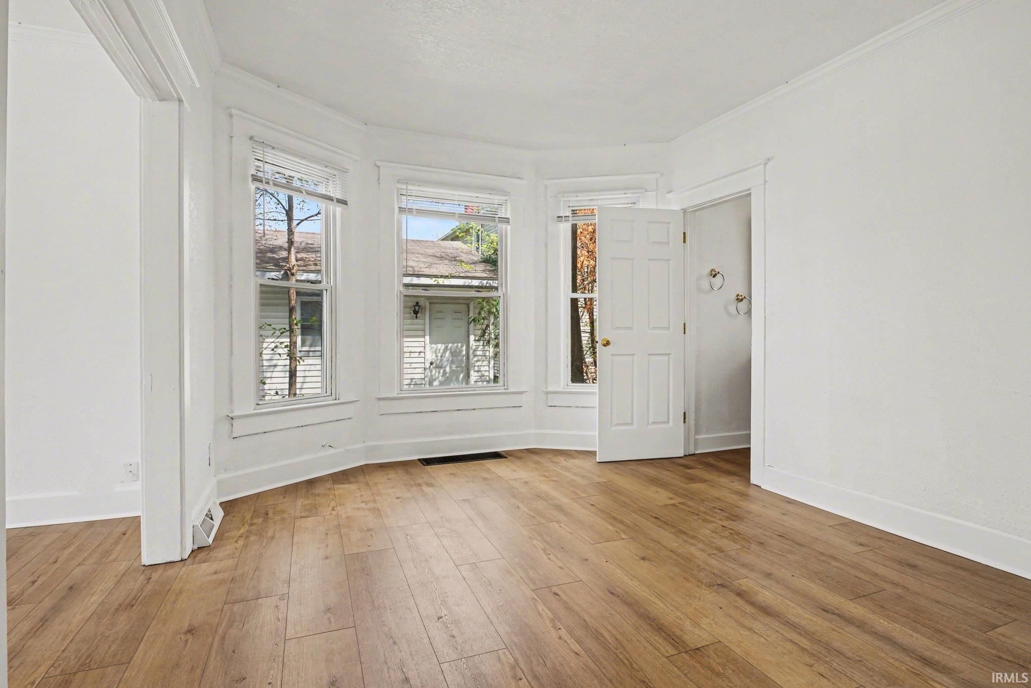 Bay window with three double-hung windows, wood-finish flooring, white trim, and a white interior door