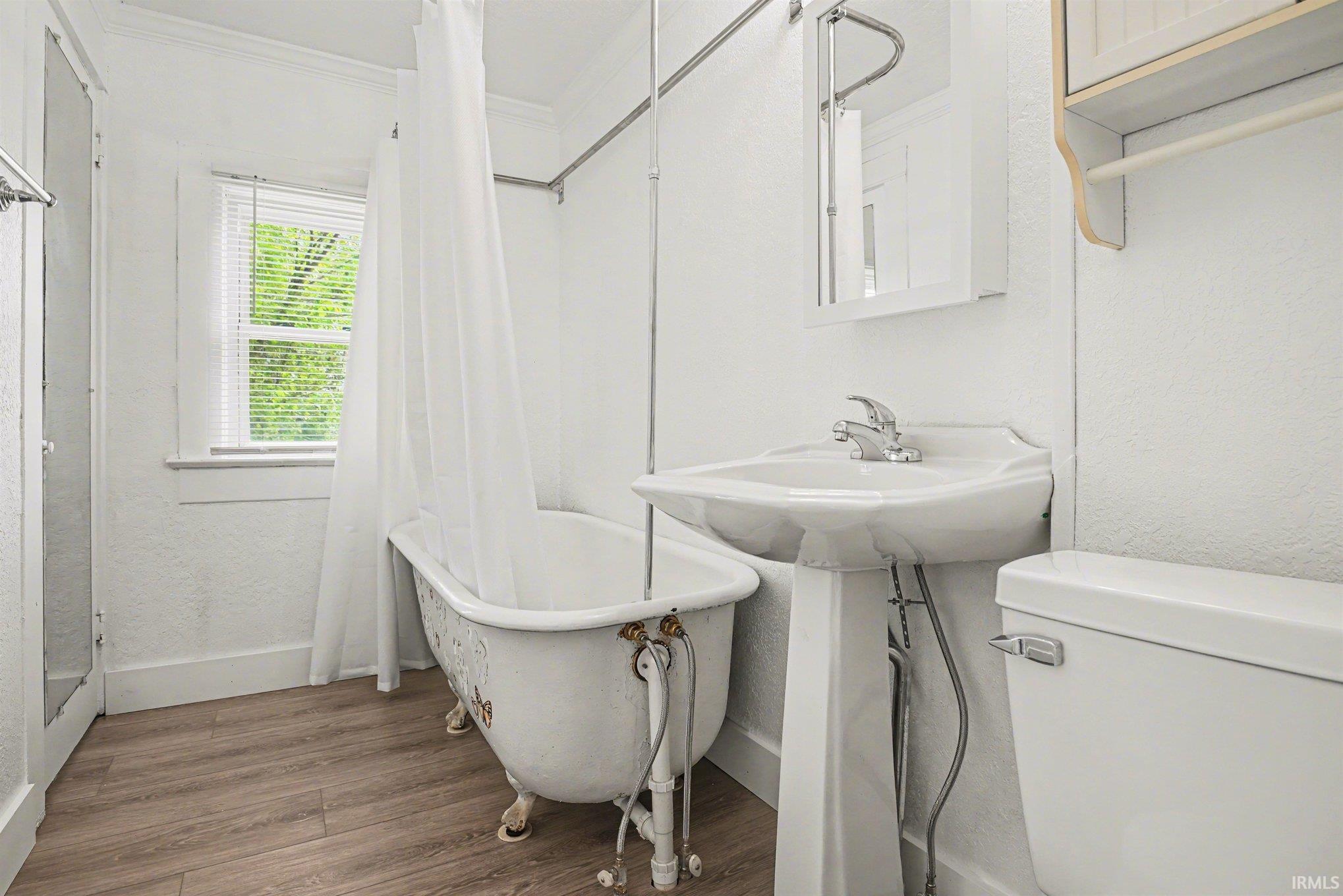 Bathroom featuring a clawfoot tub, pedestal sink, and wood-finish flooring