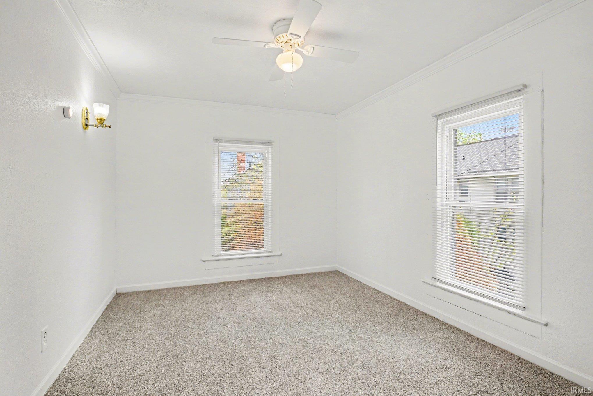 Carpeted room featuring white walls, two windows with blinds, a ceiling fan with light, and a wall-mounted sconce
