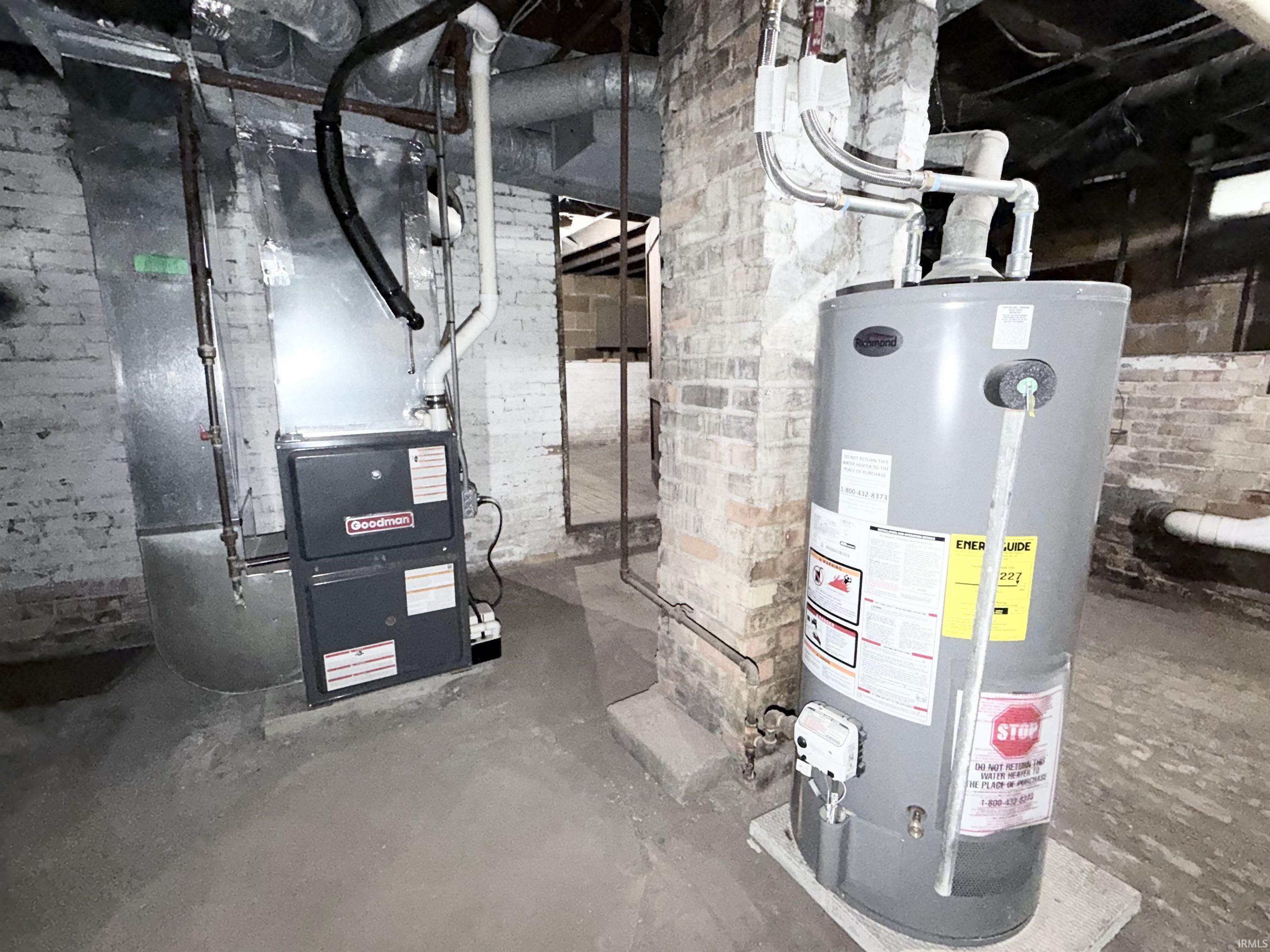 Basement utility area featuring a furnace unit, water heater, exposed brick walls, visible ductwork, and a concrete floor