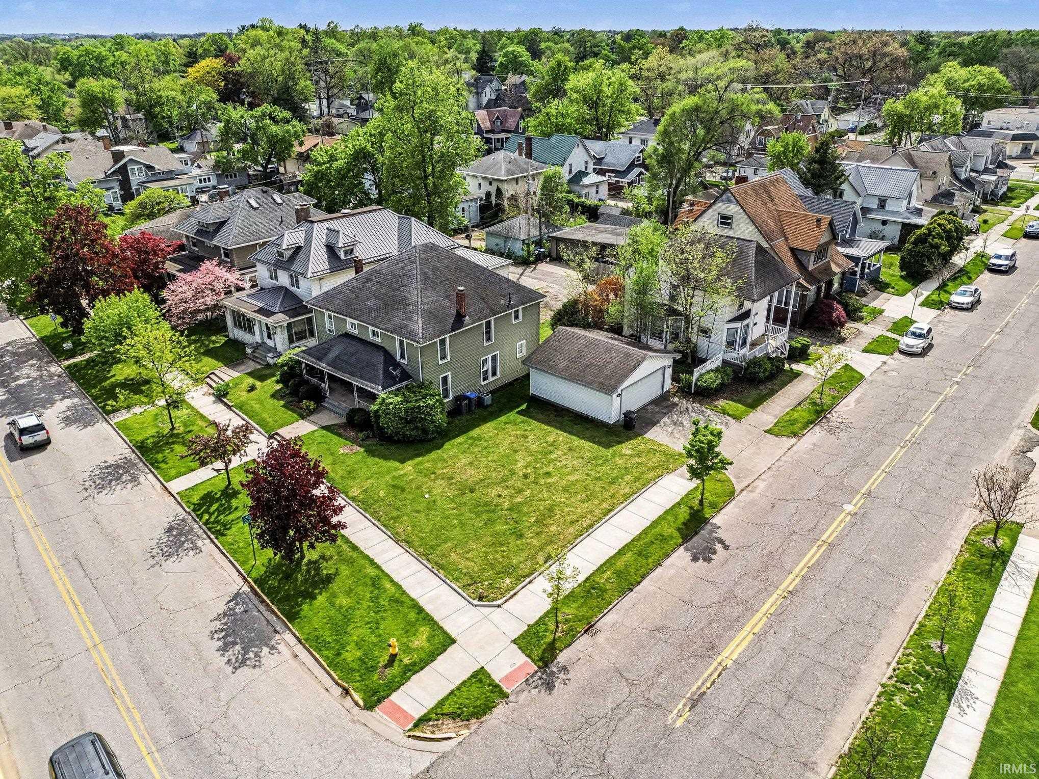Corner lot property featuring a light green exterior, dark shingle roof, and a covered front porch