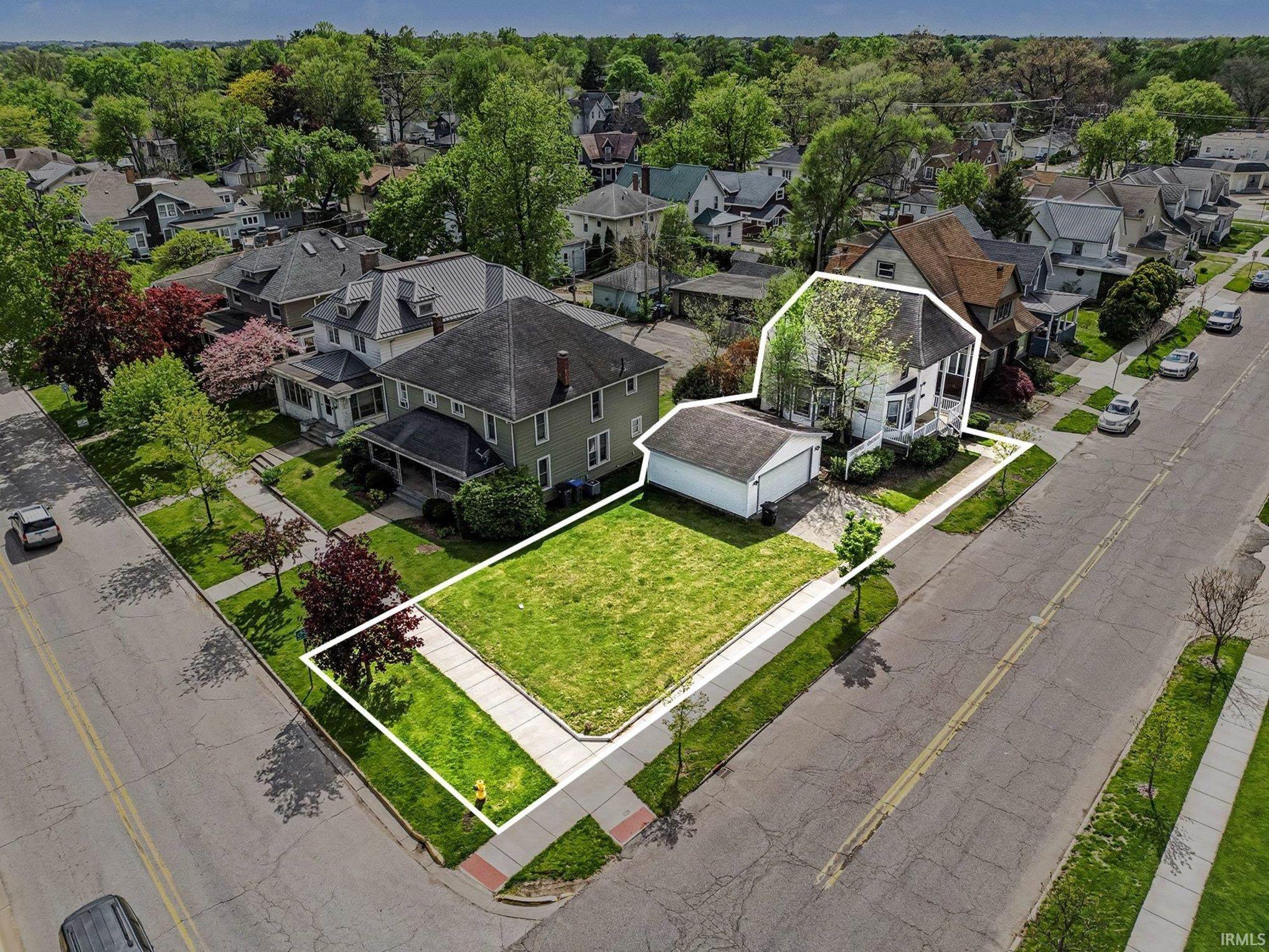 Aerial view of a residential lot featuring a detached garage and a separate adjacent lot with a green lawn