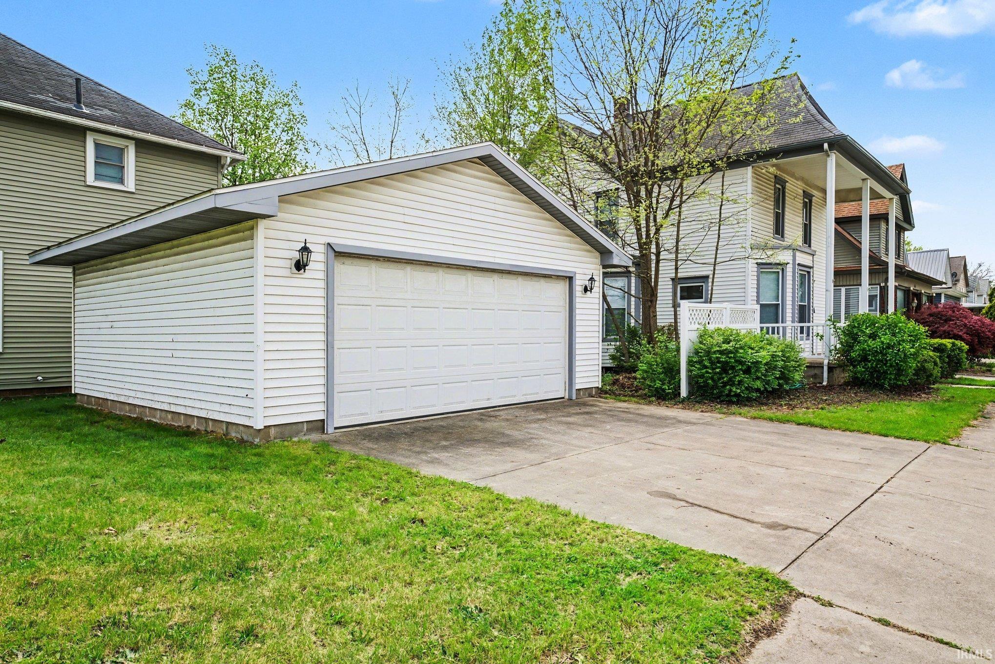 Detached garage with horizontal siding, two exterior sconces, and a concrete driveway