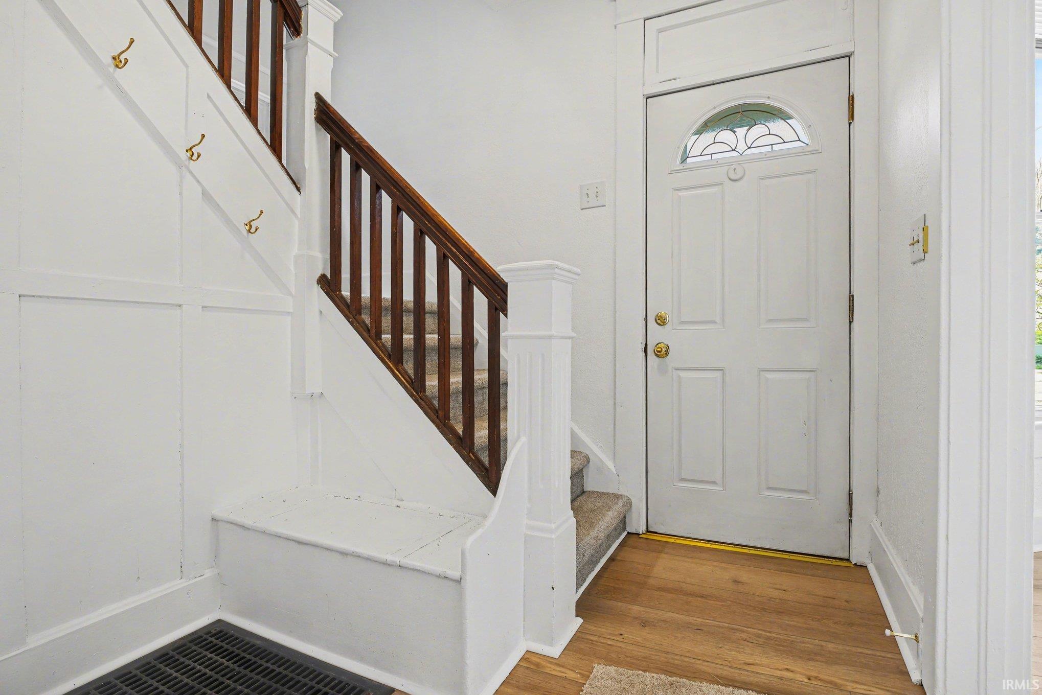 Entryway featuring a paneled door with an arched stained-glass insert, wood-finish flooring, and a staircase with dark wood railings