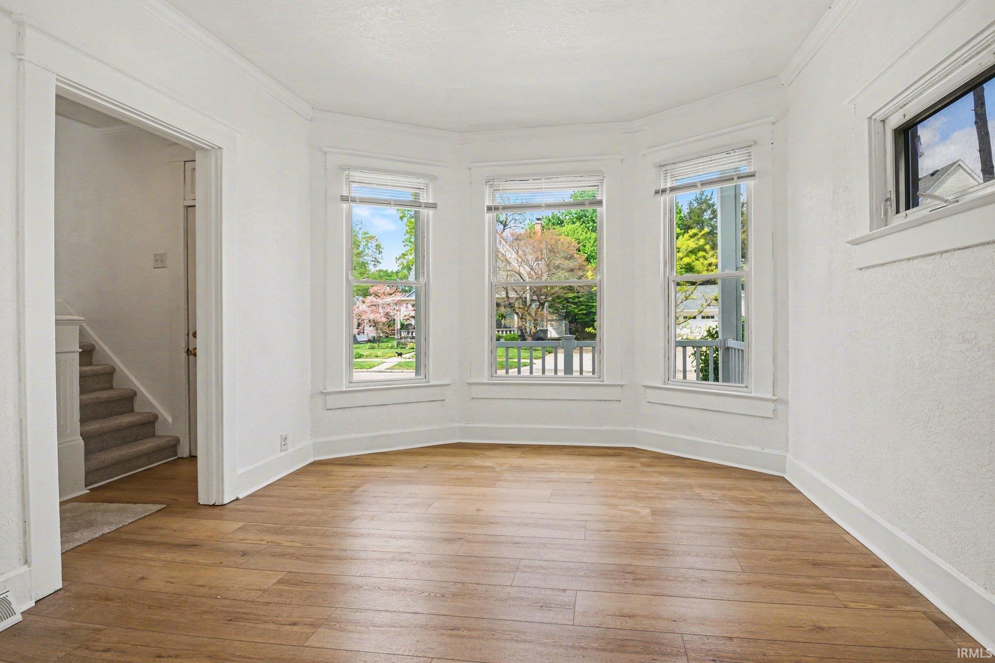 Bay window with three large windows, wood-finish flooring, white trim, and a bright white wall finish