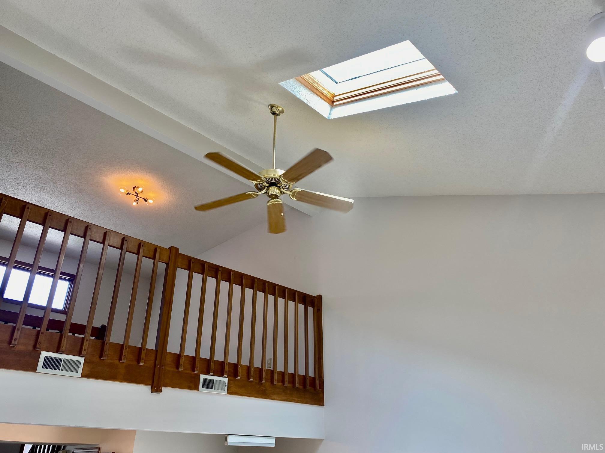 Vaulted ceiling featuring a skylight, a ceiling fan with light, and a built-in wooden railing system