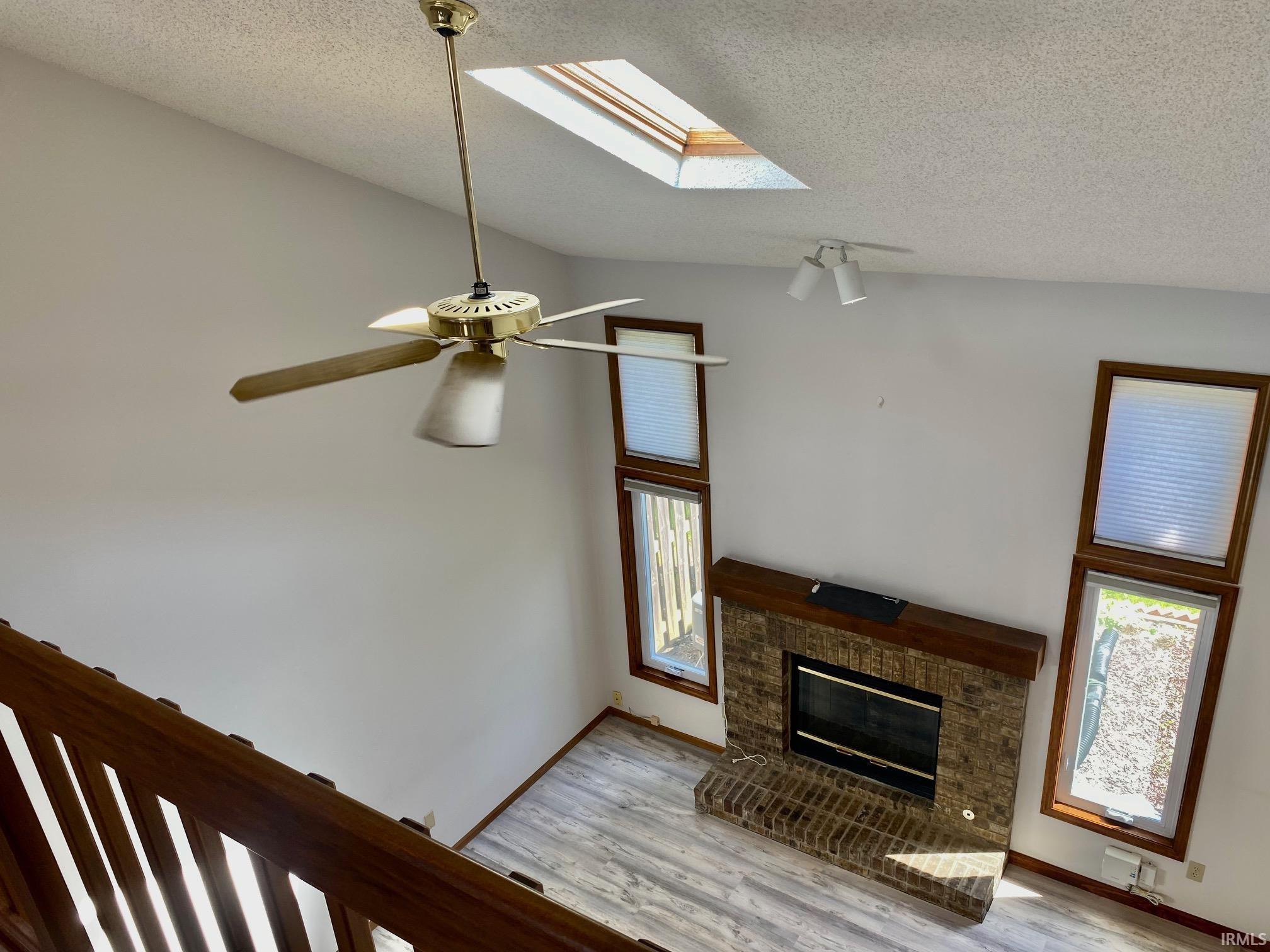 Vaulted ceiling living space featuring a brick fireplace with a wood mantle, wood-finish flooring, and multiple windows