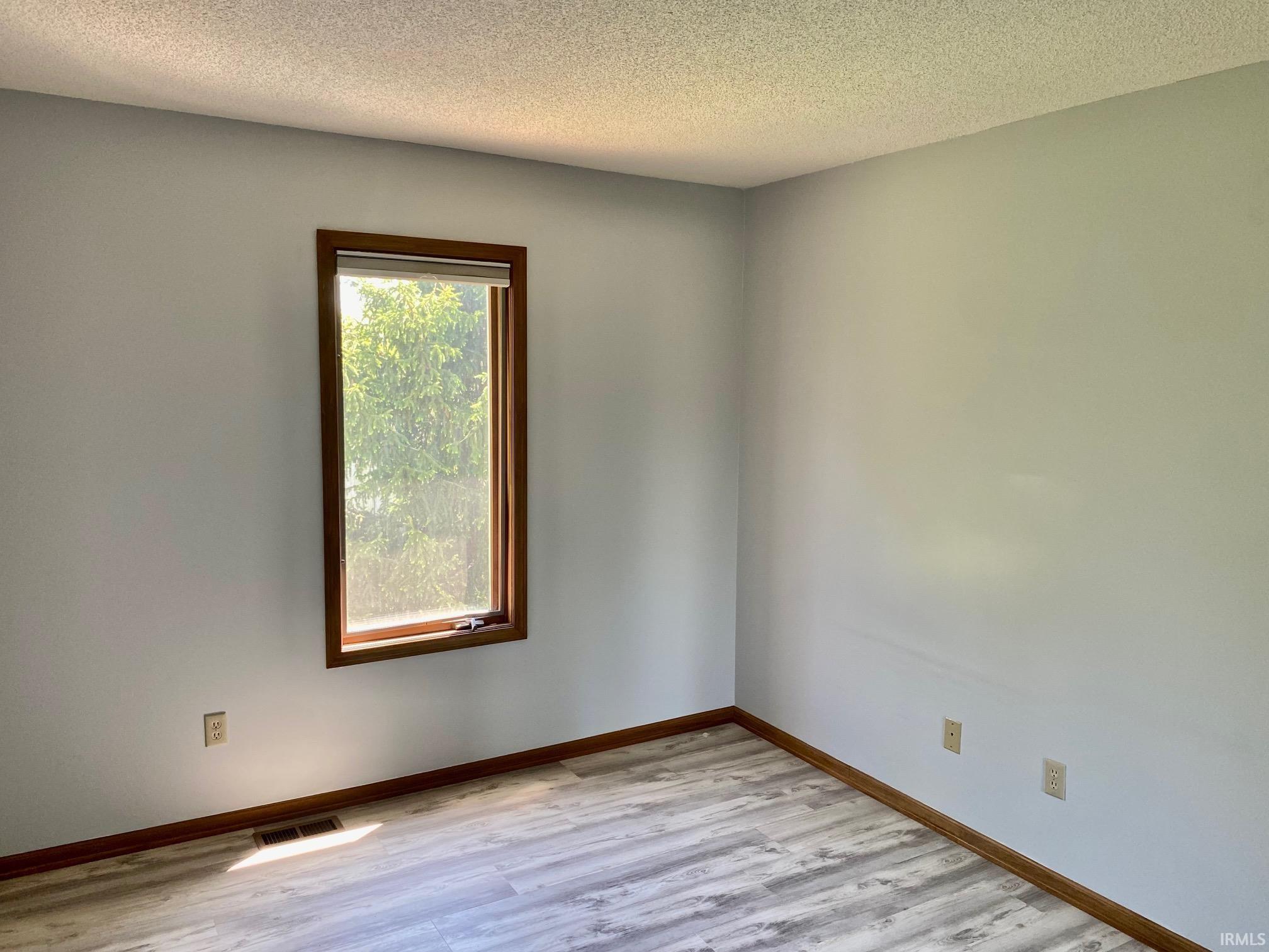Room with wood-finish flooring, light gray walls, and a window featuring natural wood trim