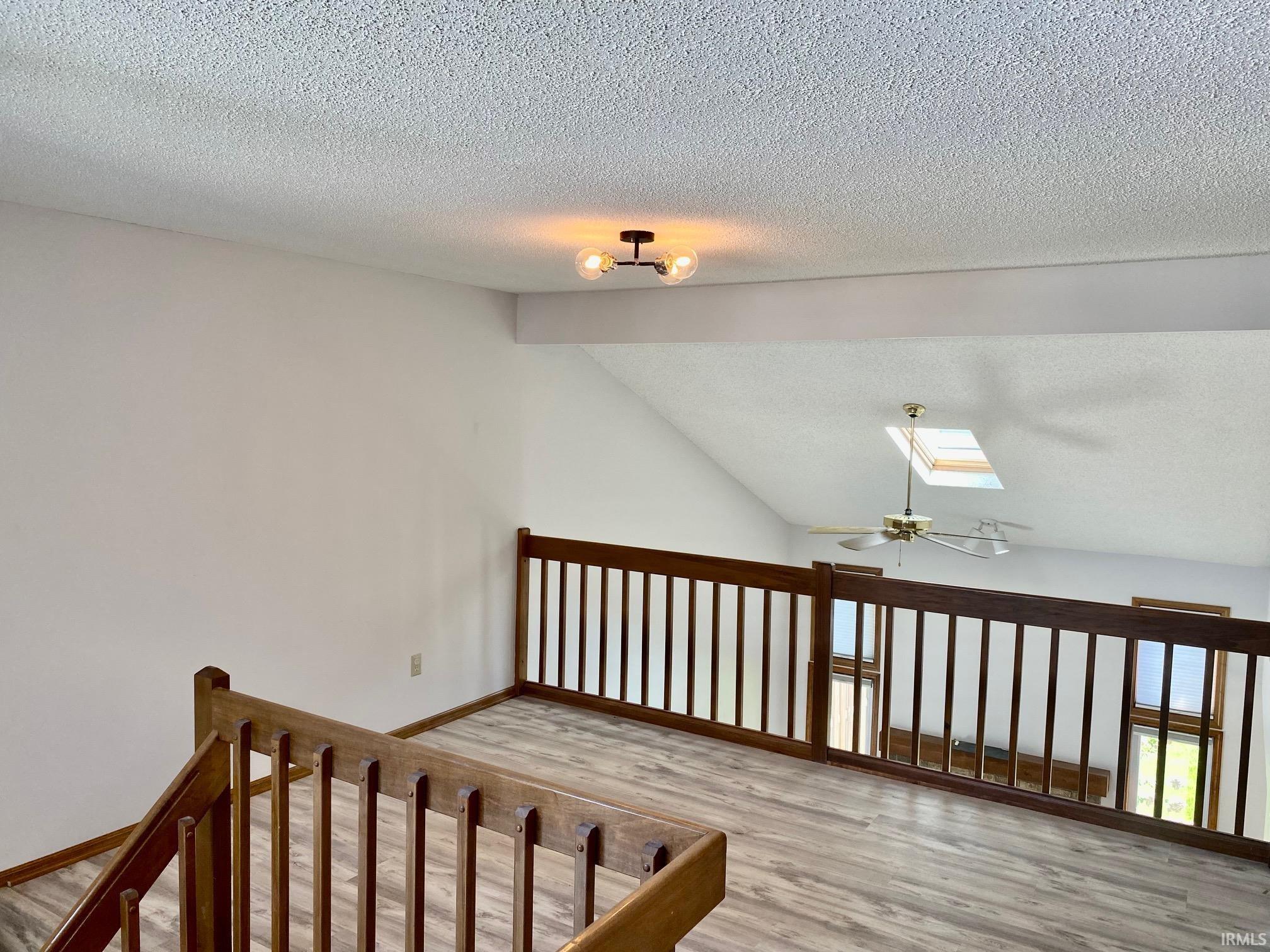 Upper-level loft with wood-finish flooring, featuring a dark wood railing, vaulted ceiling, and a skylight