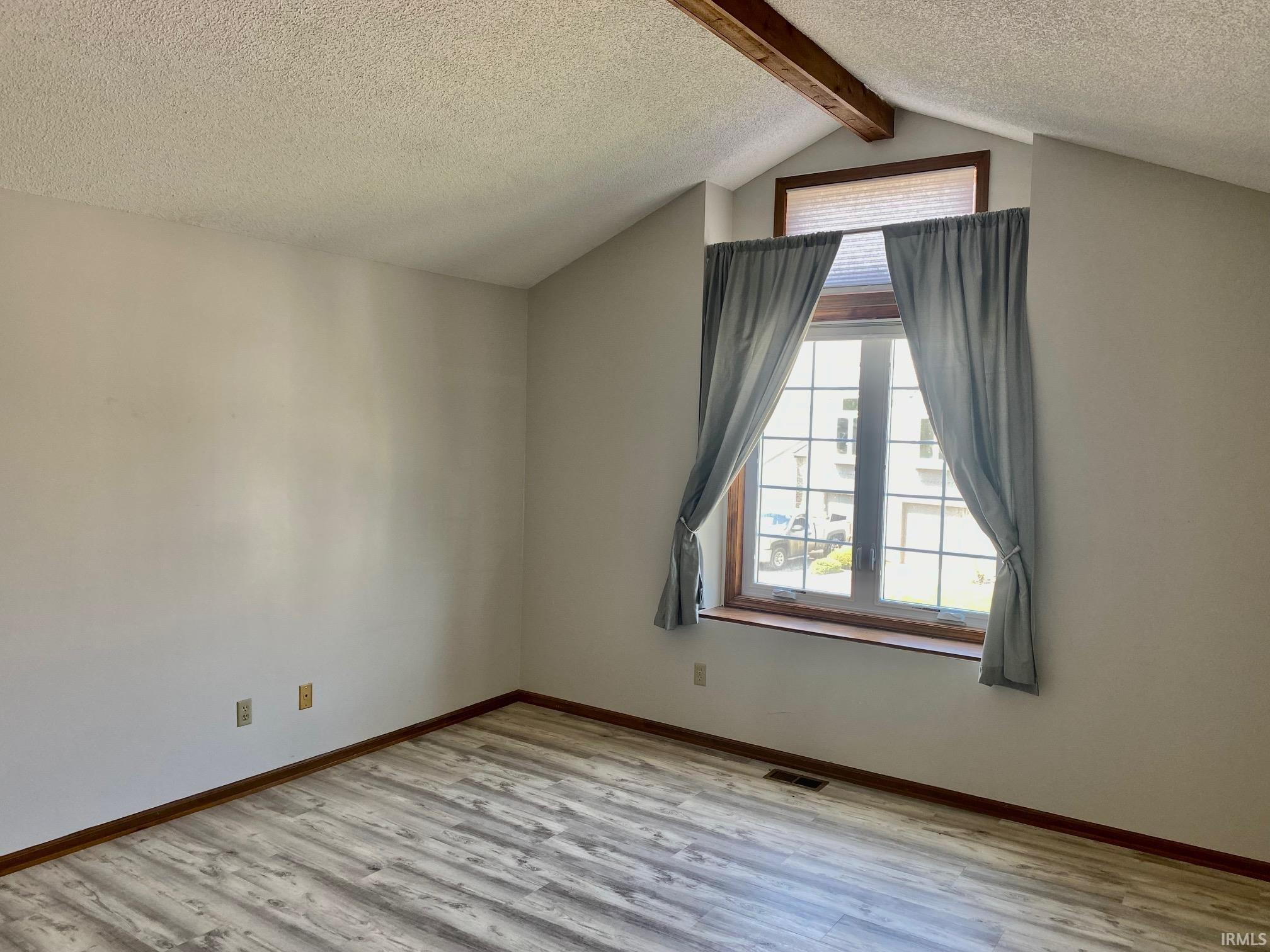 Slanted ceiling featuring exposed wood beams, window with mullions, and wood-finish flooring