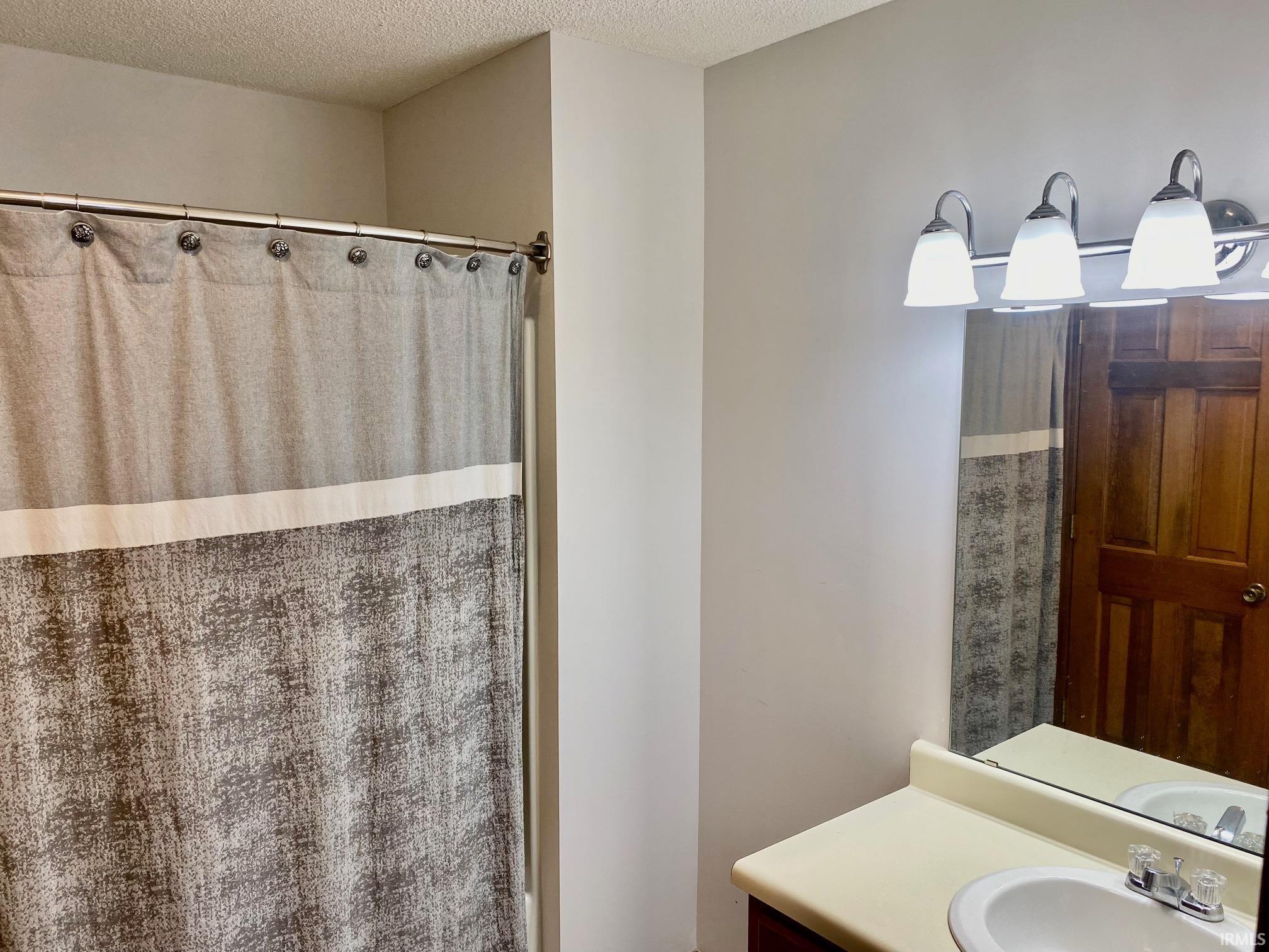 Bathroom vanity featuring a single basin sink, integrated countertop, and wall-mounted light fixture with three sconces