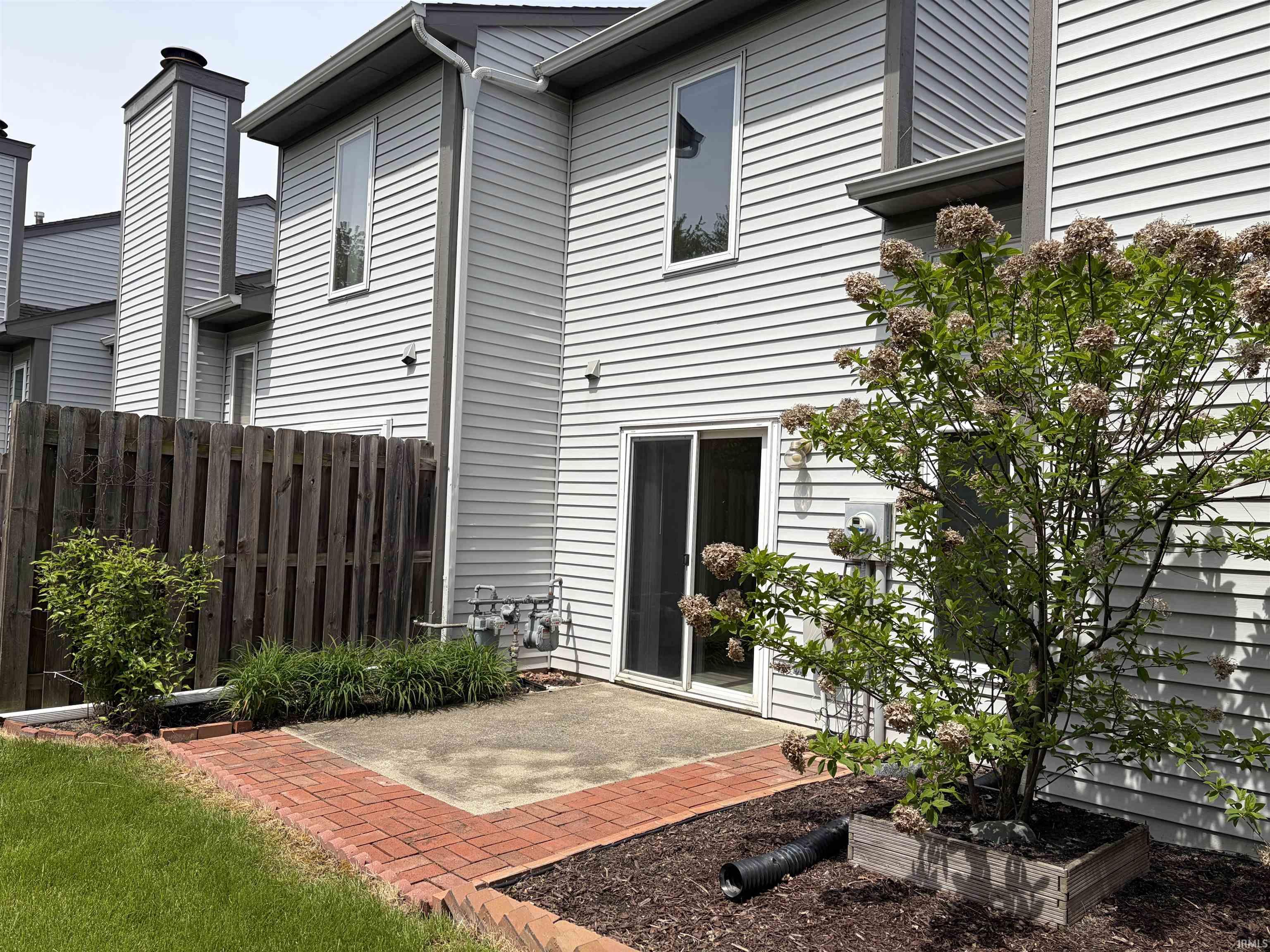 Private patio area featuring brick edging, a sliding glass door, and a wooden privacy fence