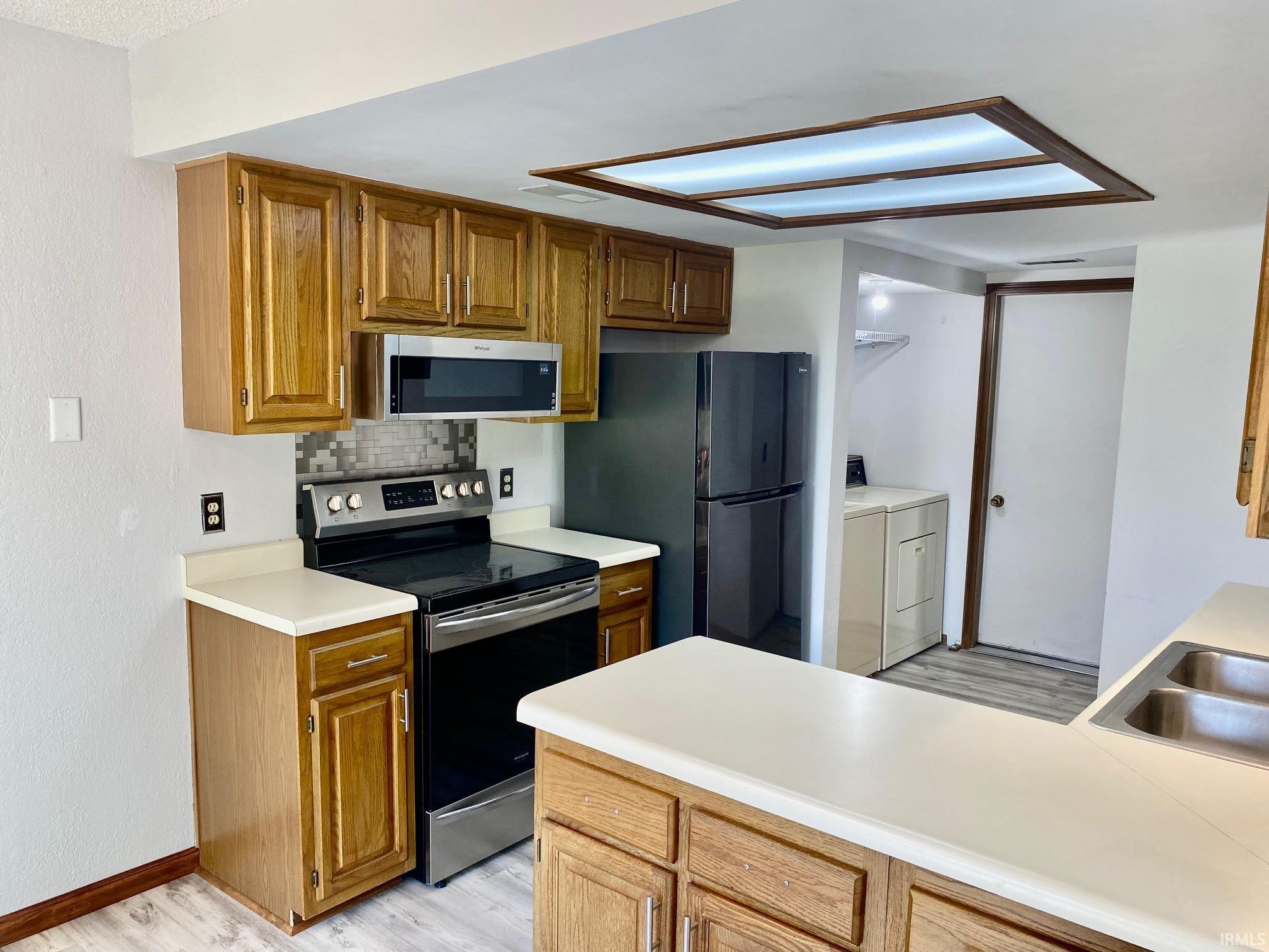 Kitchen featuring wood cabinetry, light-toned countertops, and a full suite of stainless steel appliances