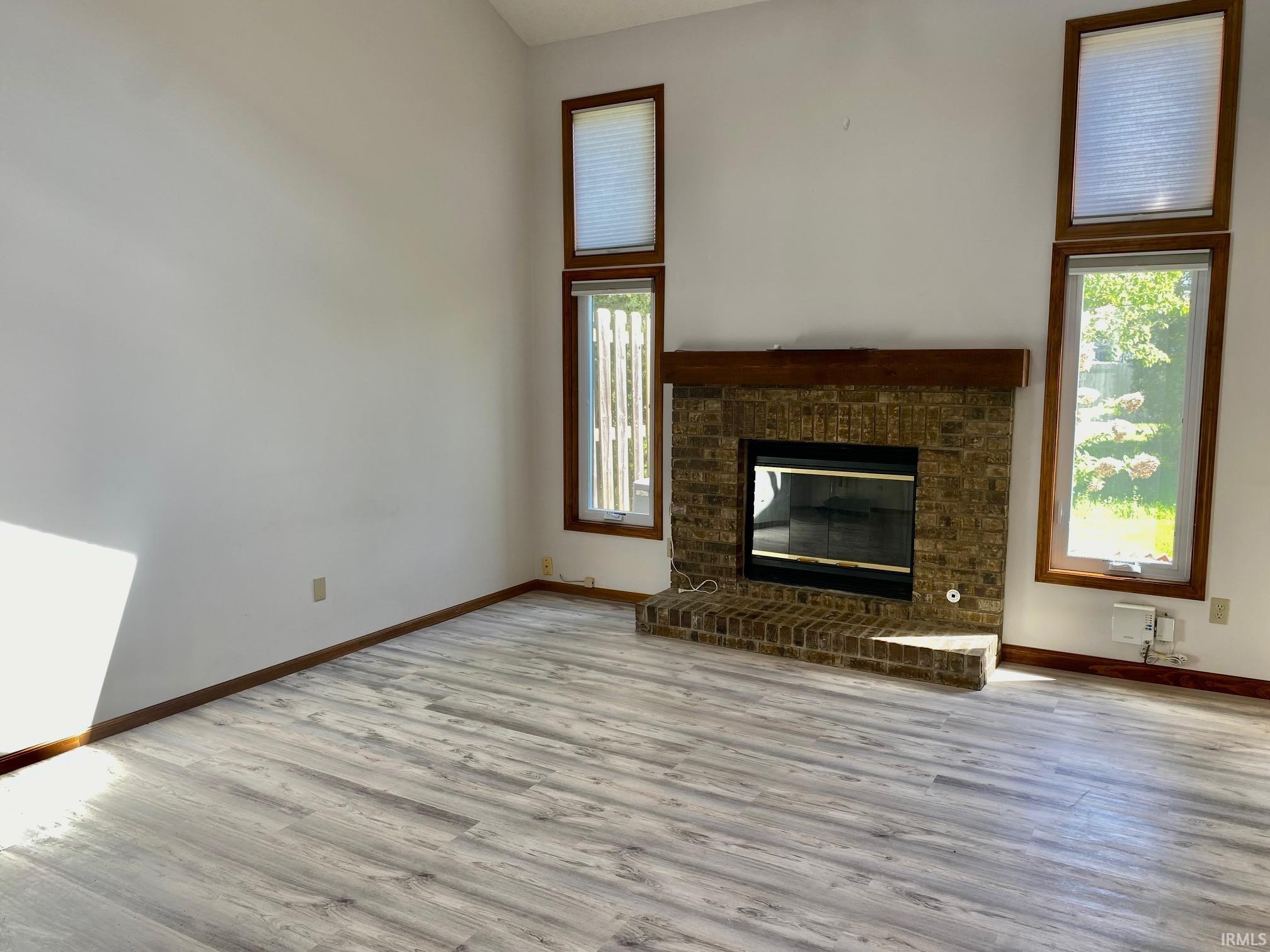 Living area featuring a brick fireplace with a wood mantle, wood-finish flooring, and multiple windows with wood frames