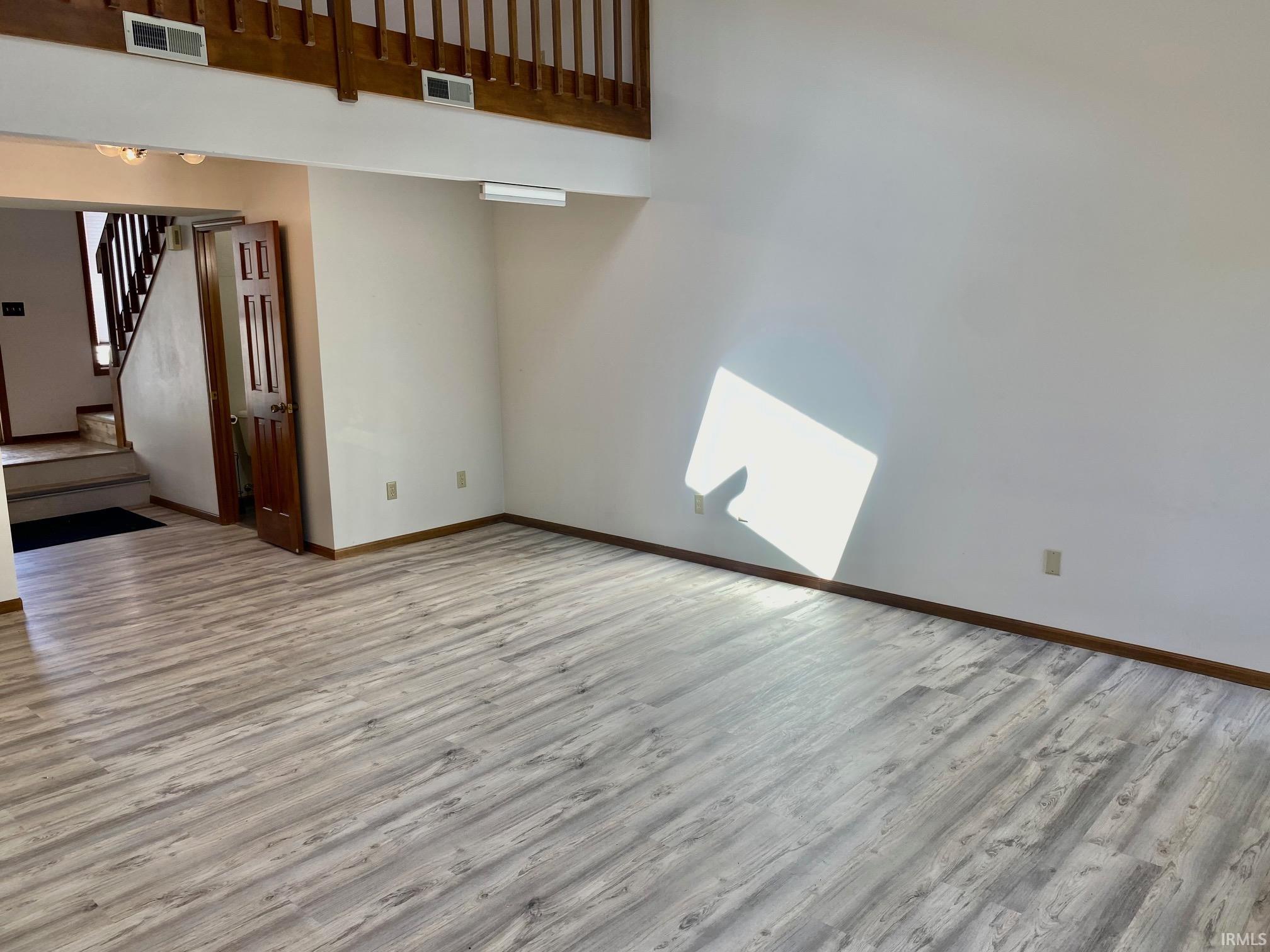 Spacious interior featuring wood-finish flooring, white walls, and a visible second-story railing