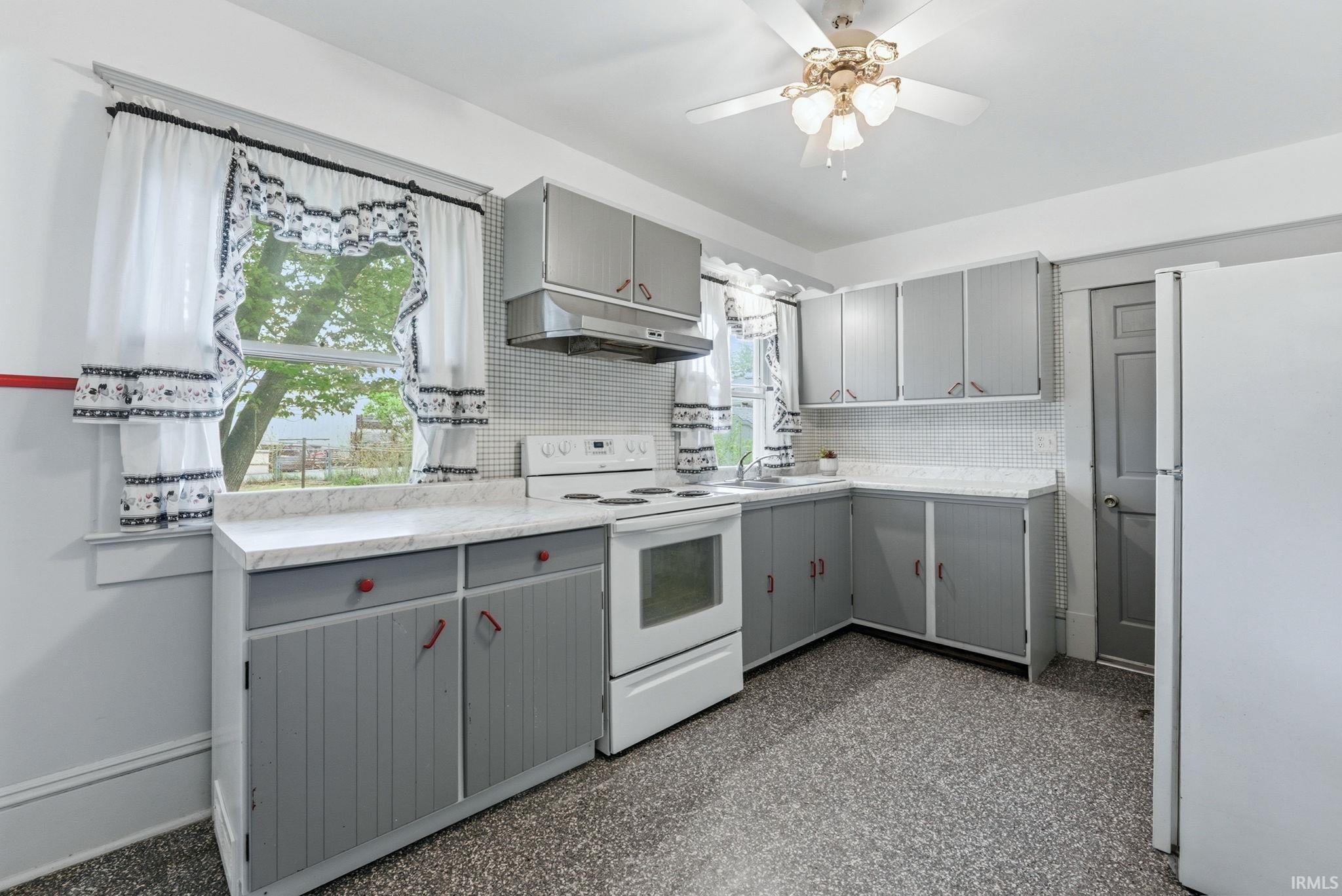 Kitchen featuring a window, white appliances, grey cabinetry with red hardware, light-toned countertops, and a ceiling fan