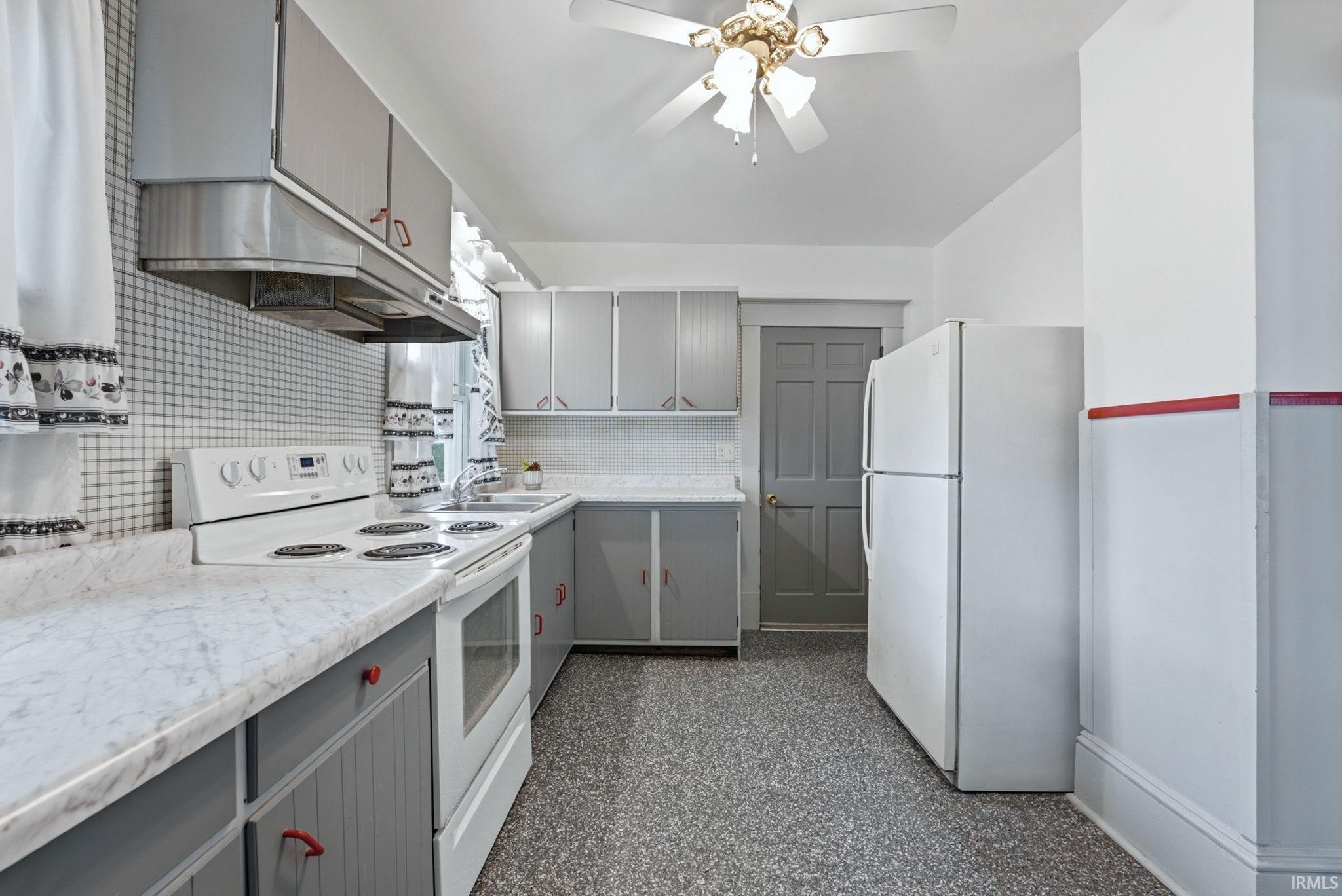 Kitchen featuring grey cabinetry with red pulls, white appliances, and a tiled backsplash