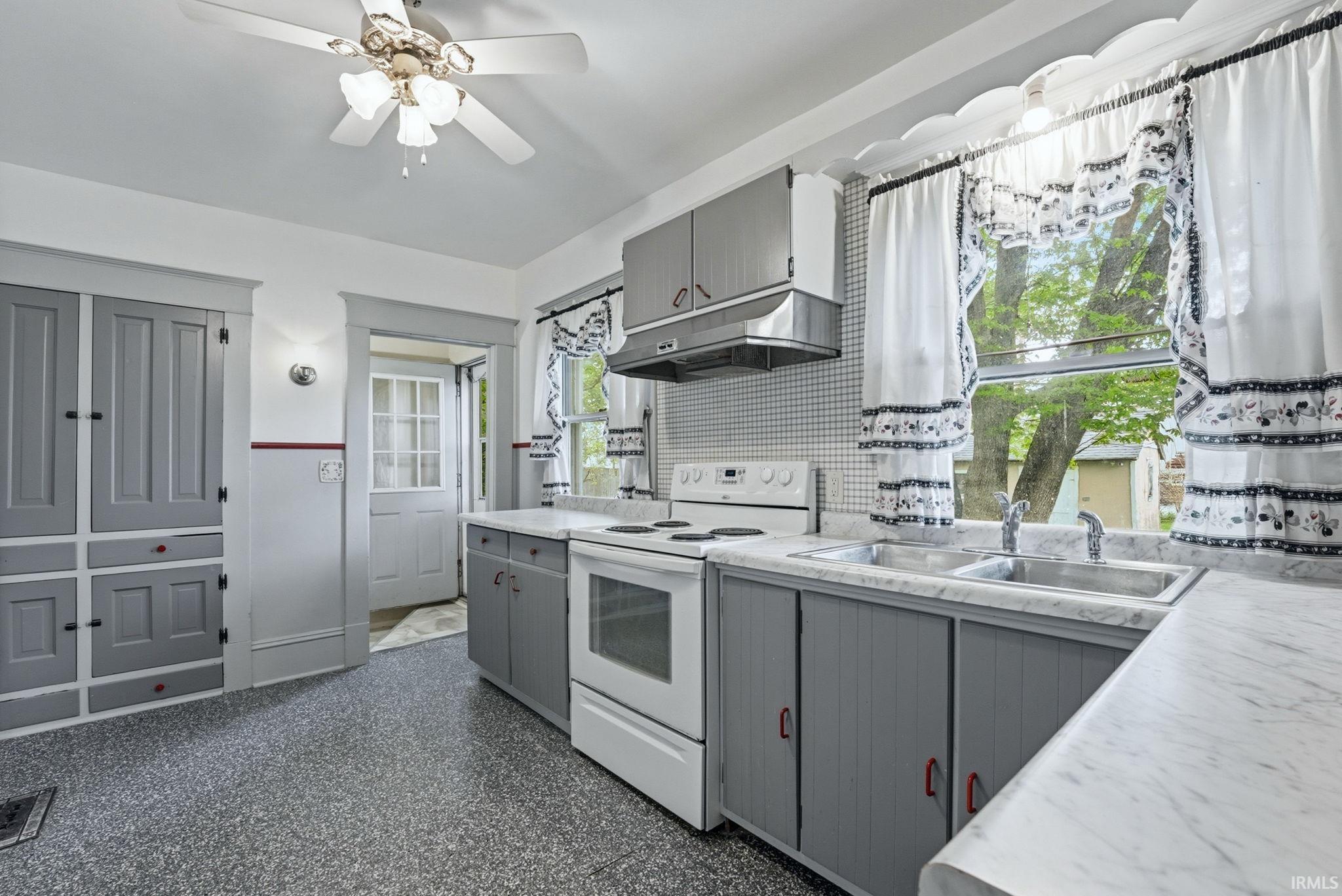 Kitchen featuring white appliances, a double basin sink, gray cabinetry, speckled flooring, and a ceiling fan