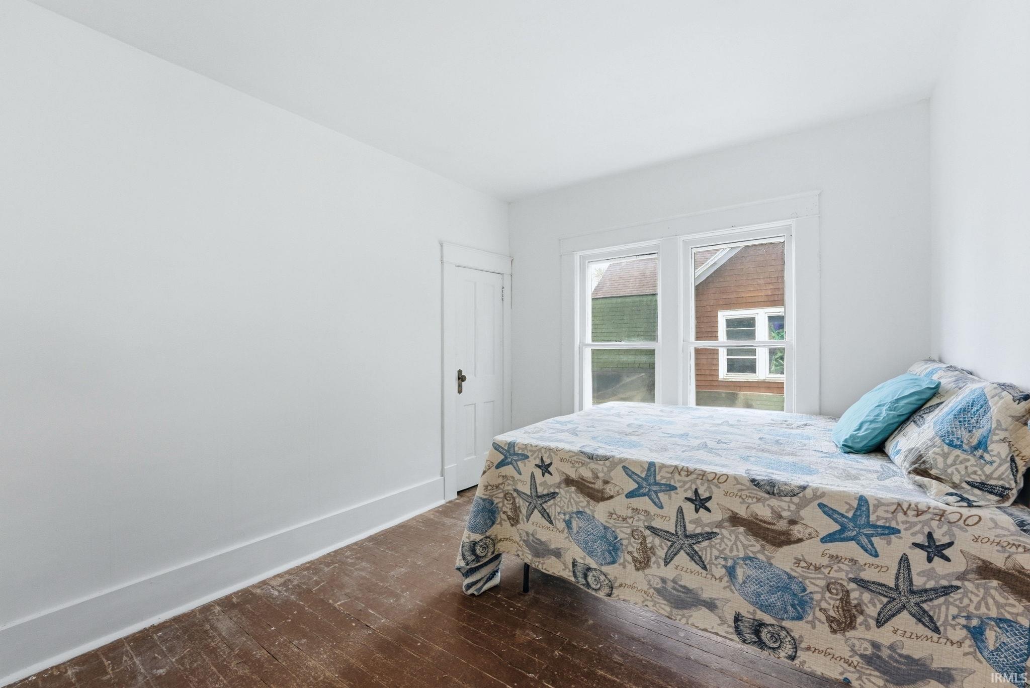 Bedroom featuring wood-finish flooring, white walls, and a multi-pane window