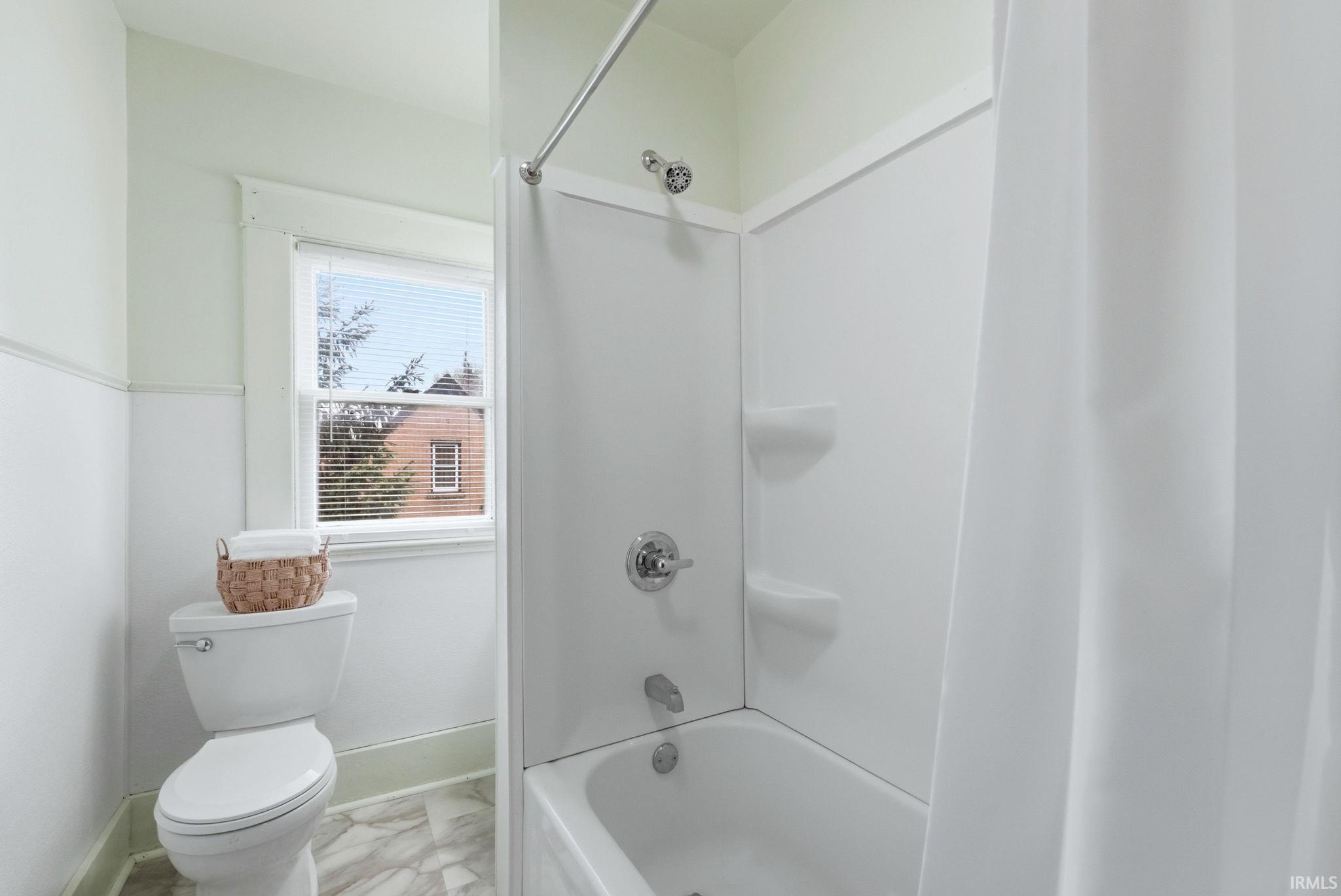 Full bathroom featuring a white tub with an integrated shower, chrome fixtures, and a window for natural light