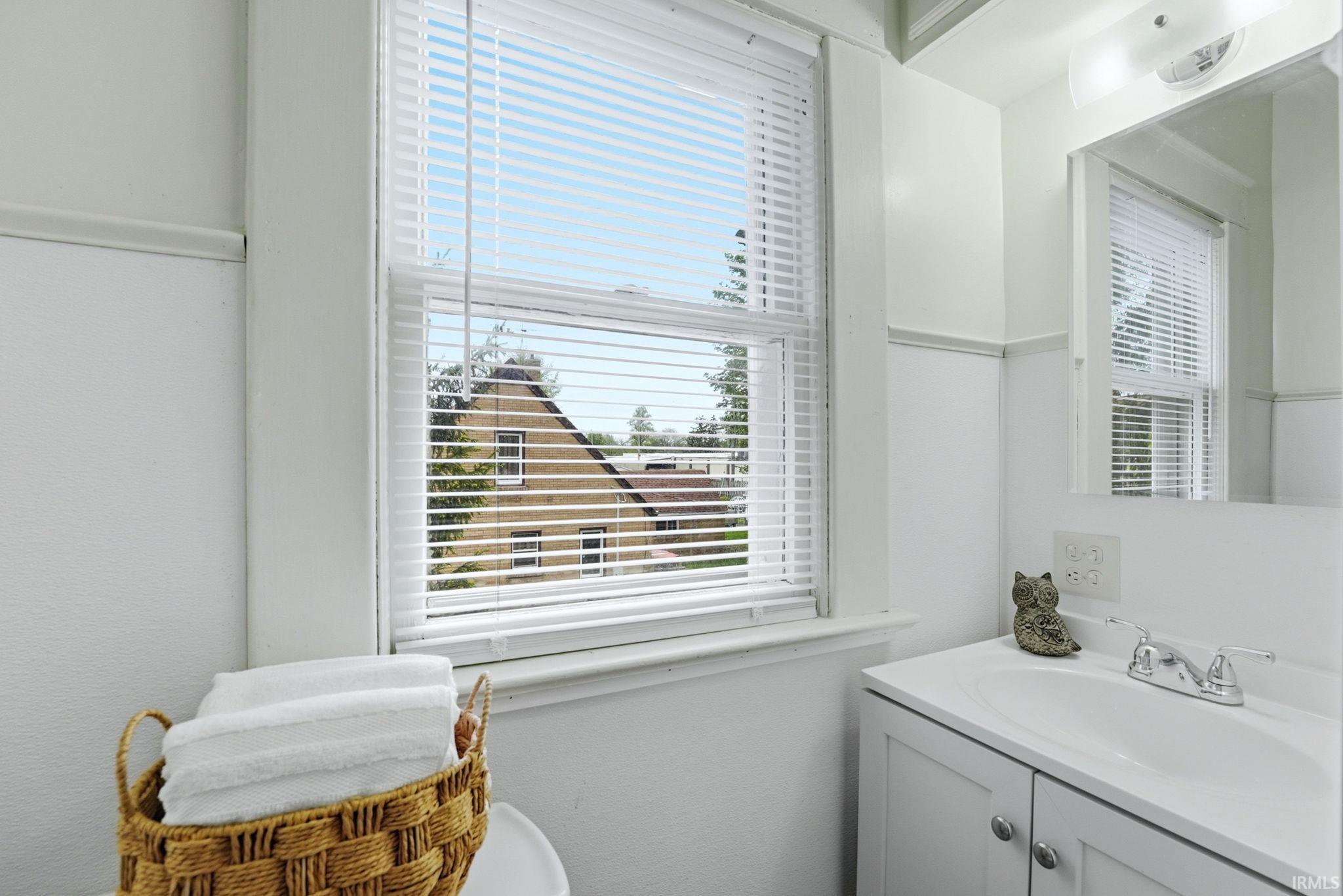 White vanity with an integrated sink and chrome faucet, featuring a large mirror and overhead lighting
