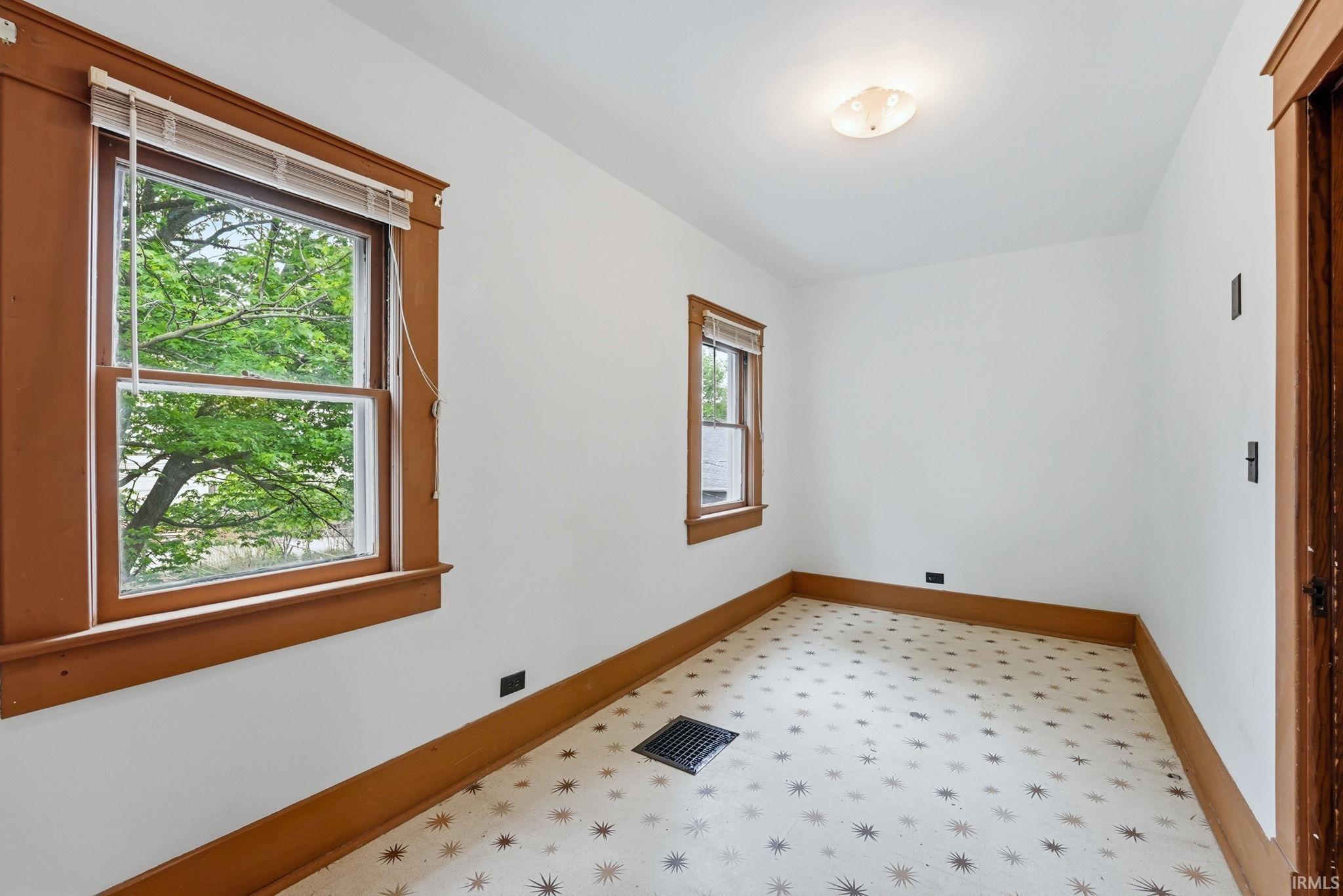 Compact room featuring two windows with wood trim, a patterned flooring surface, and a flush-mount ceiling light fixture