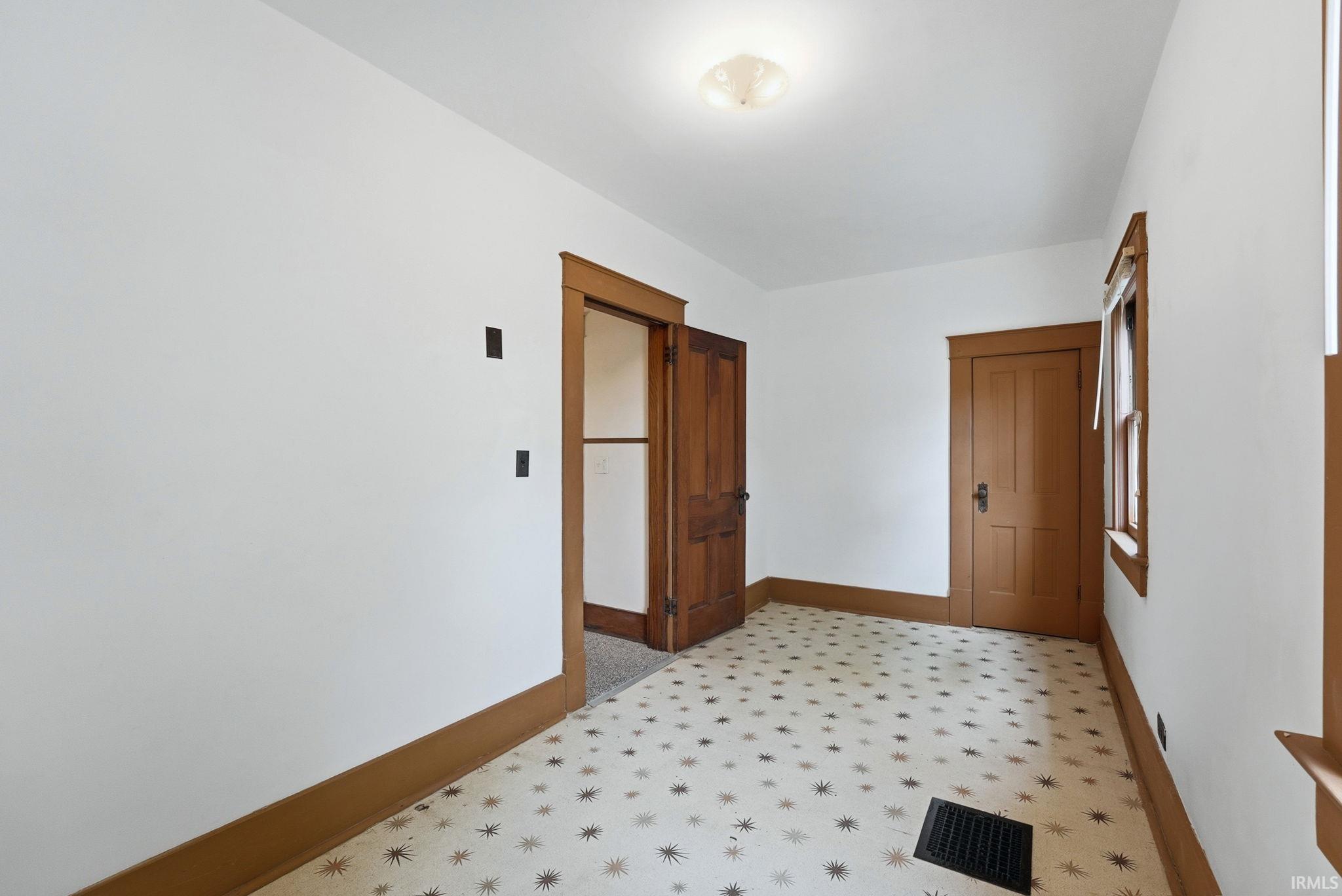 Room featuring patterned floor tile, white walls, and wood-finish trim