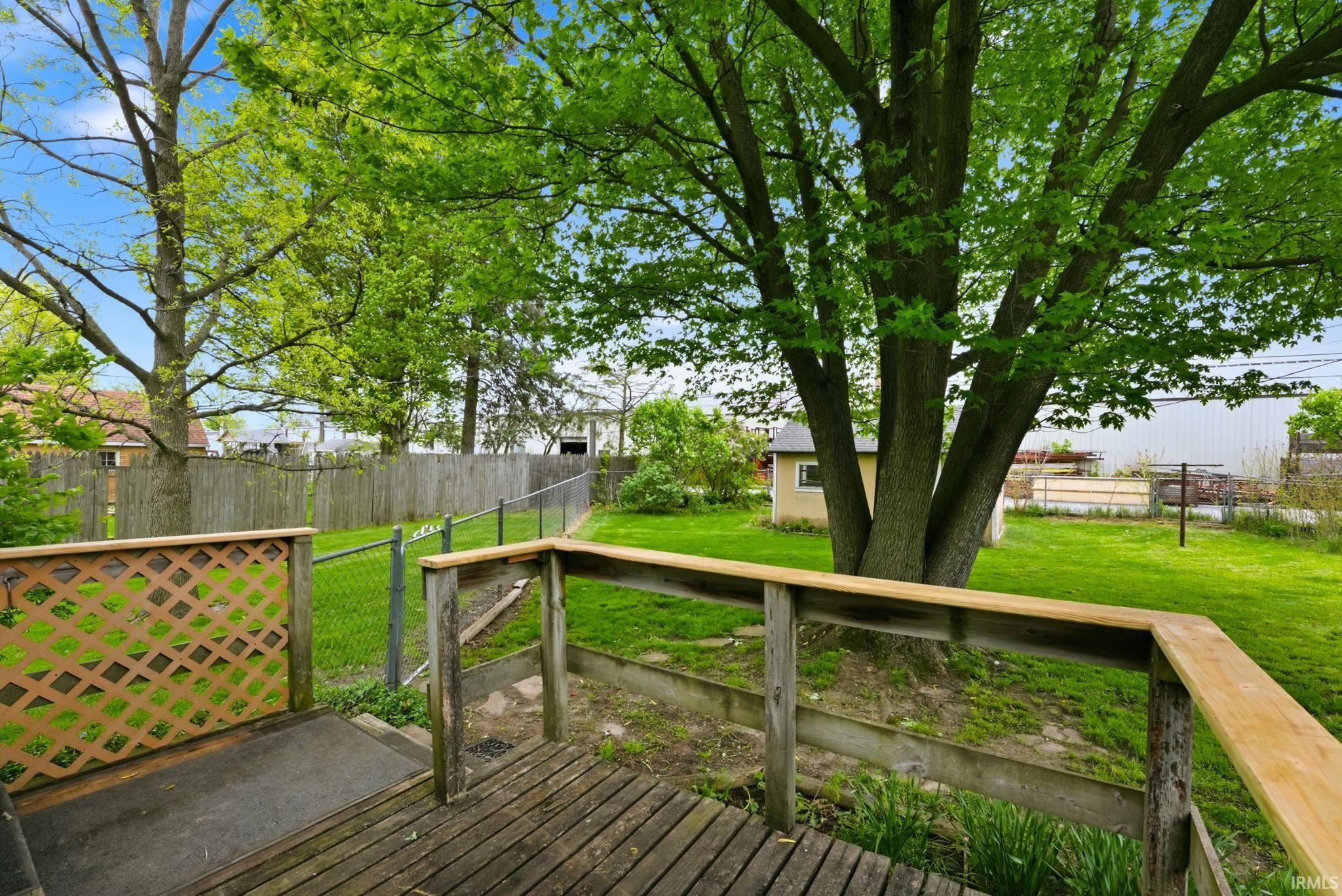 Rear yard featuring a wood deck with lattice and railing, a large mature tree, and a detached shed