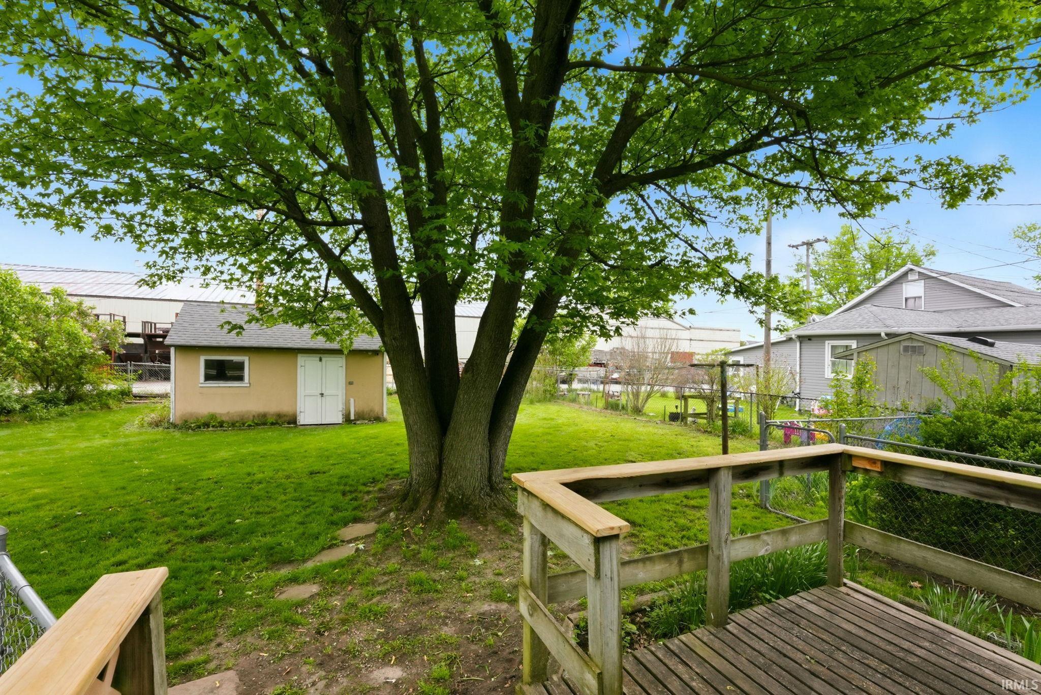 Spacious backyard featuring a wood deck, mature shade tree, and a detached storage shed with a shingled roof and double entry doors
