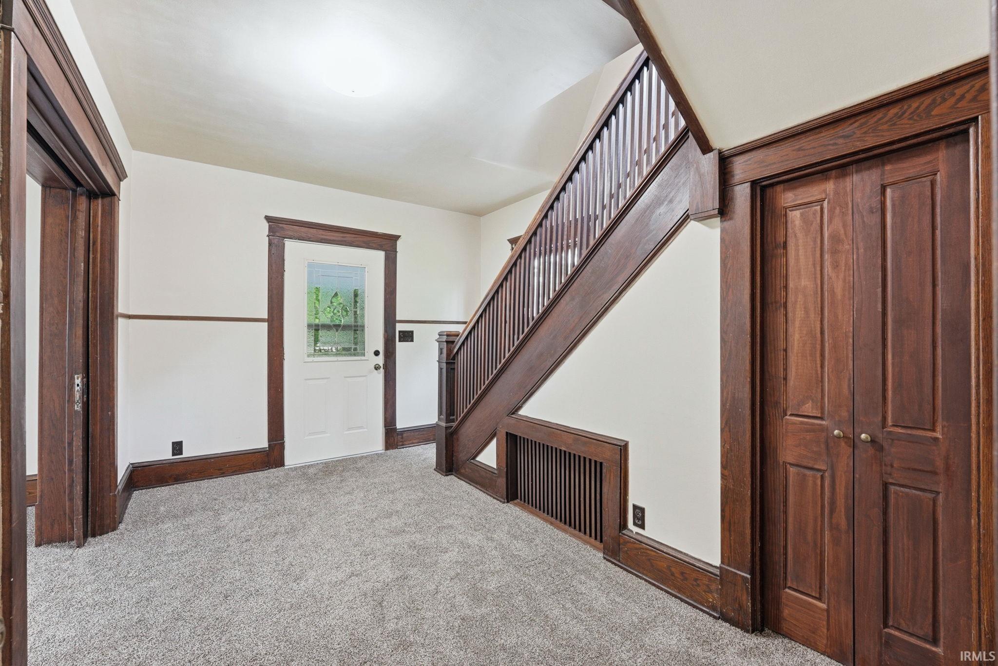 Entryway featuring a staircase with wood-finish balusters and handrail, rich wood-finish trim, a paneled door with glass insert, and neutral carpeting