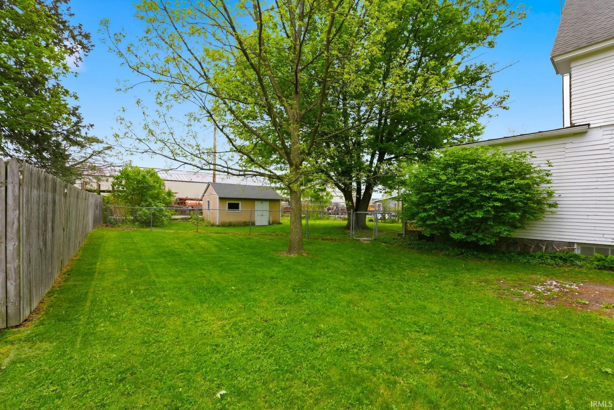 Expansive backyard featuring a green lawn, mature trees, a wooden privacy fence, a chain-link fence, and a detached storage shed