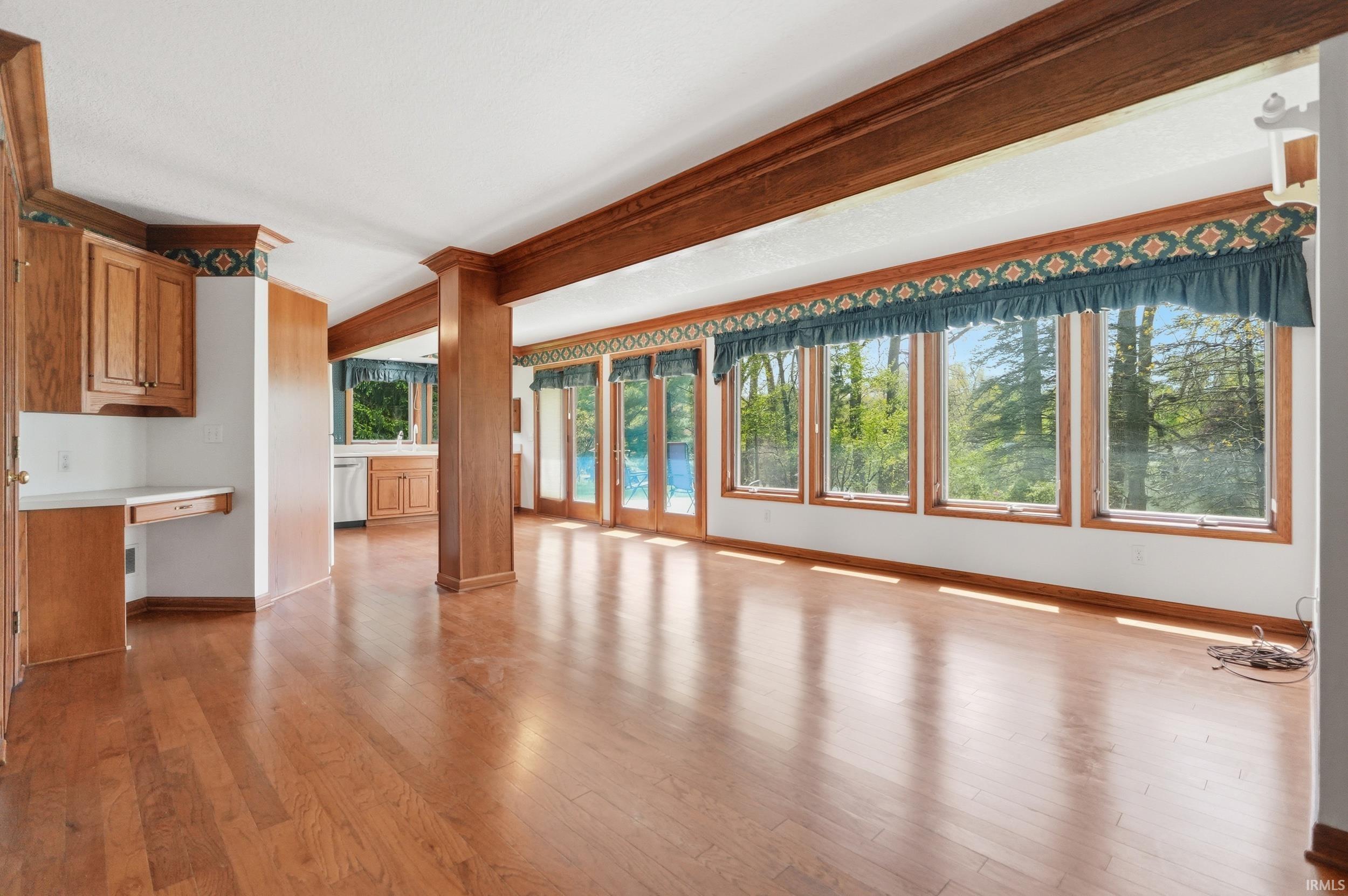 Expansive room featuring wood-finish flooring, wood structural beams, and built-in cabinetry