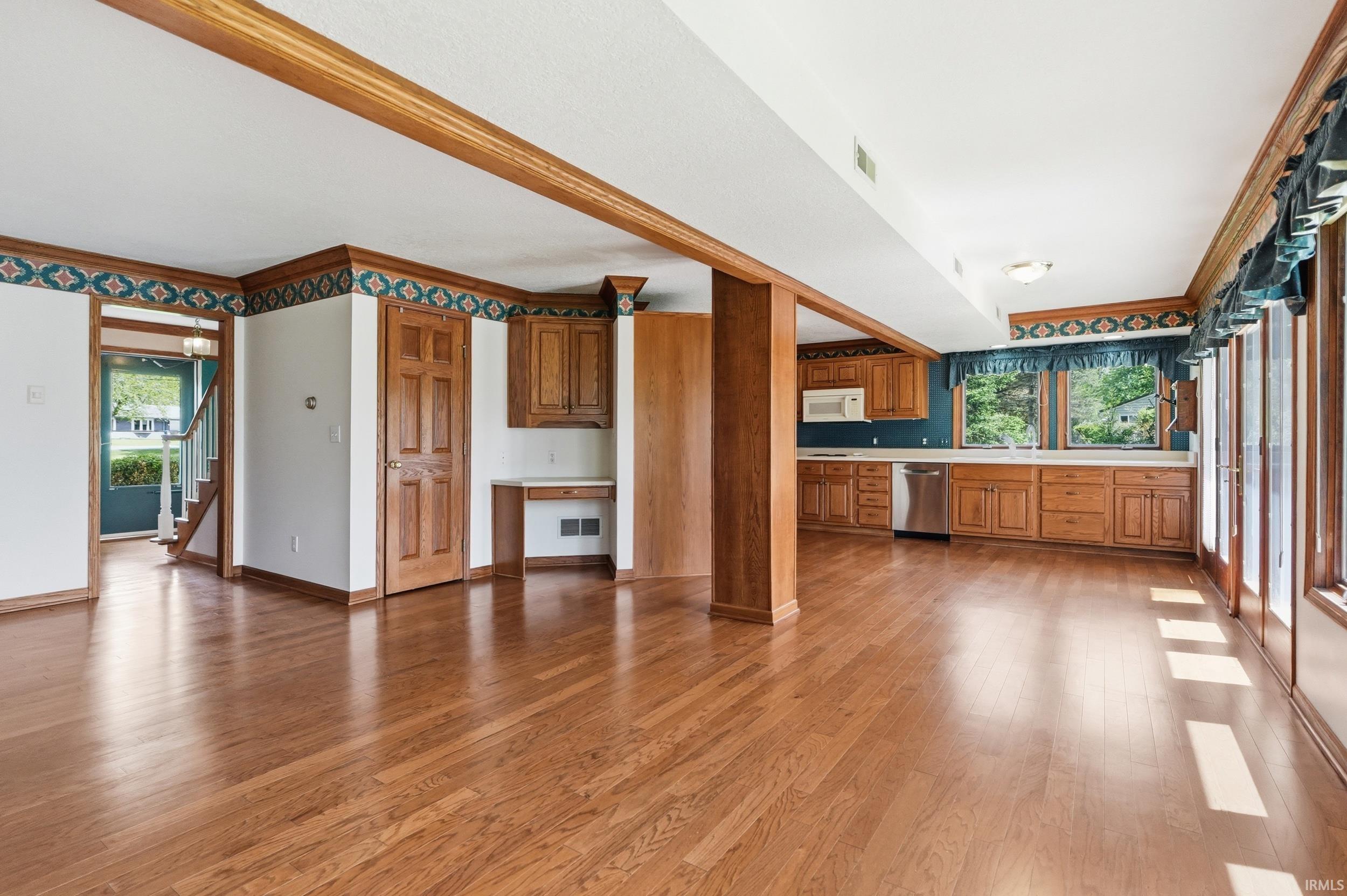Spacious open-concept room featuring wide plank wood-finish flooring, a full kitchen with wood cabinetry and stainless steel appliances, and a built-in desk area
