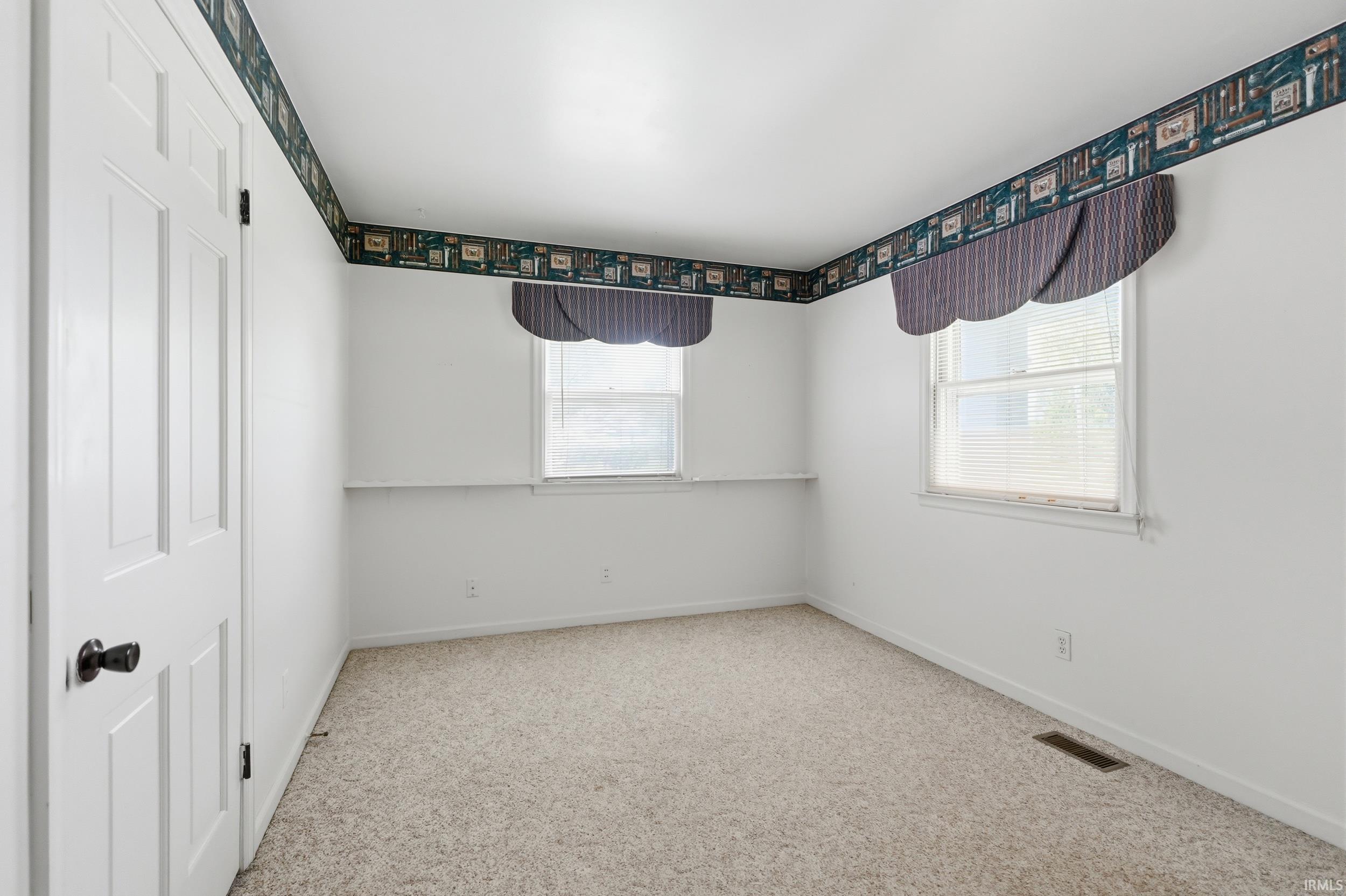 Carpeted room featuring two windows with valances and white trim, white walls, and a decorative wallpaper border