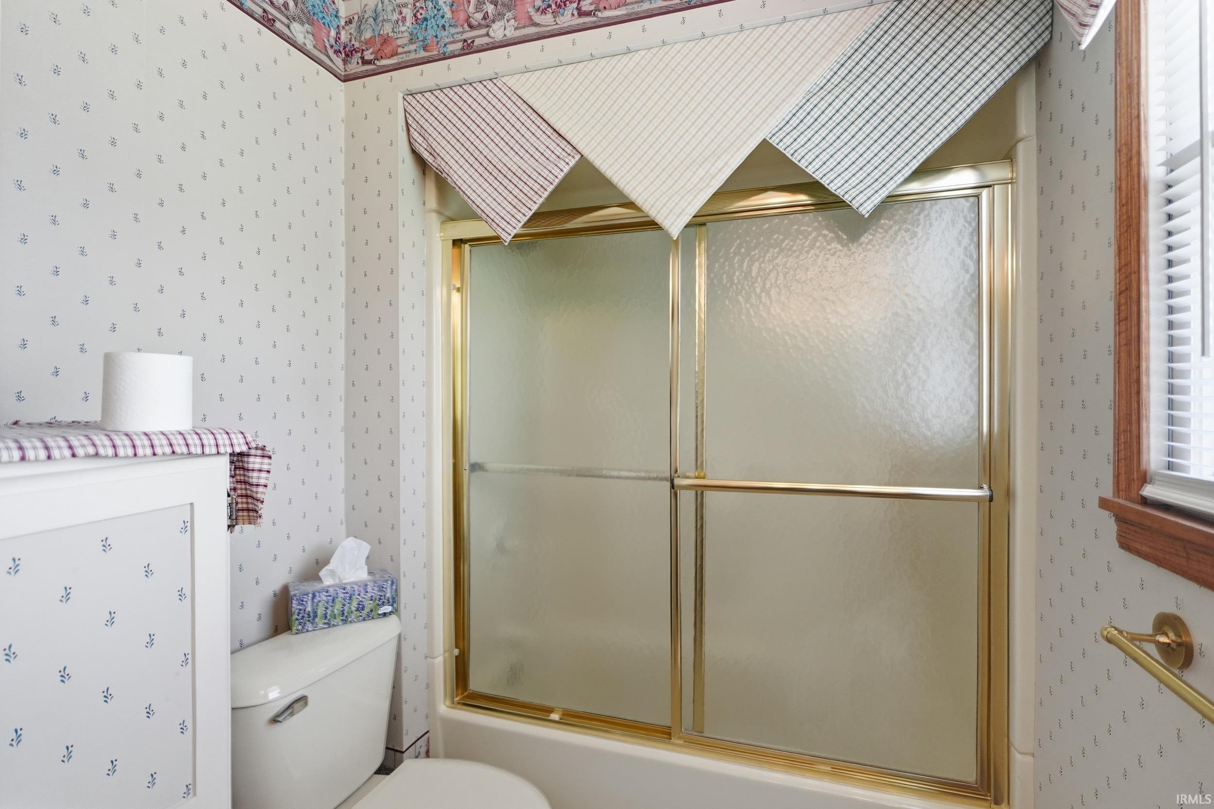 Bathroom with a gold-framed shower/tub combination featuring frosted glass sliding doors