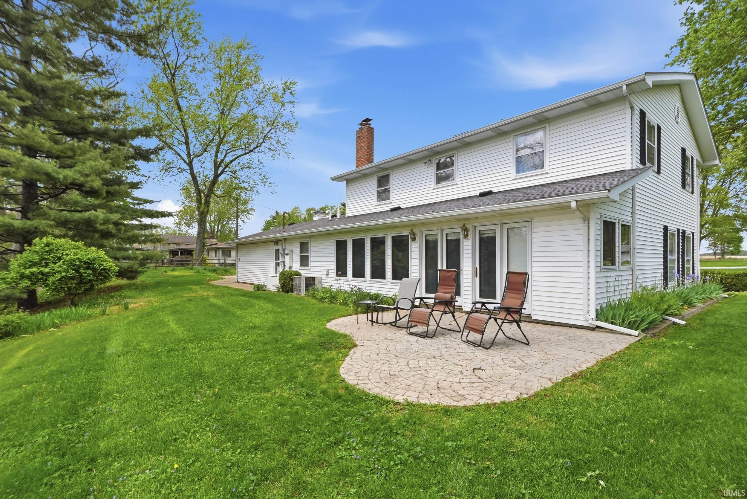 White vinyl-sided residence featuring a curved paver patio, multiple large windows, and a brick chimney