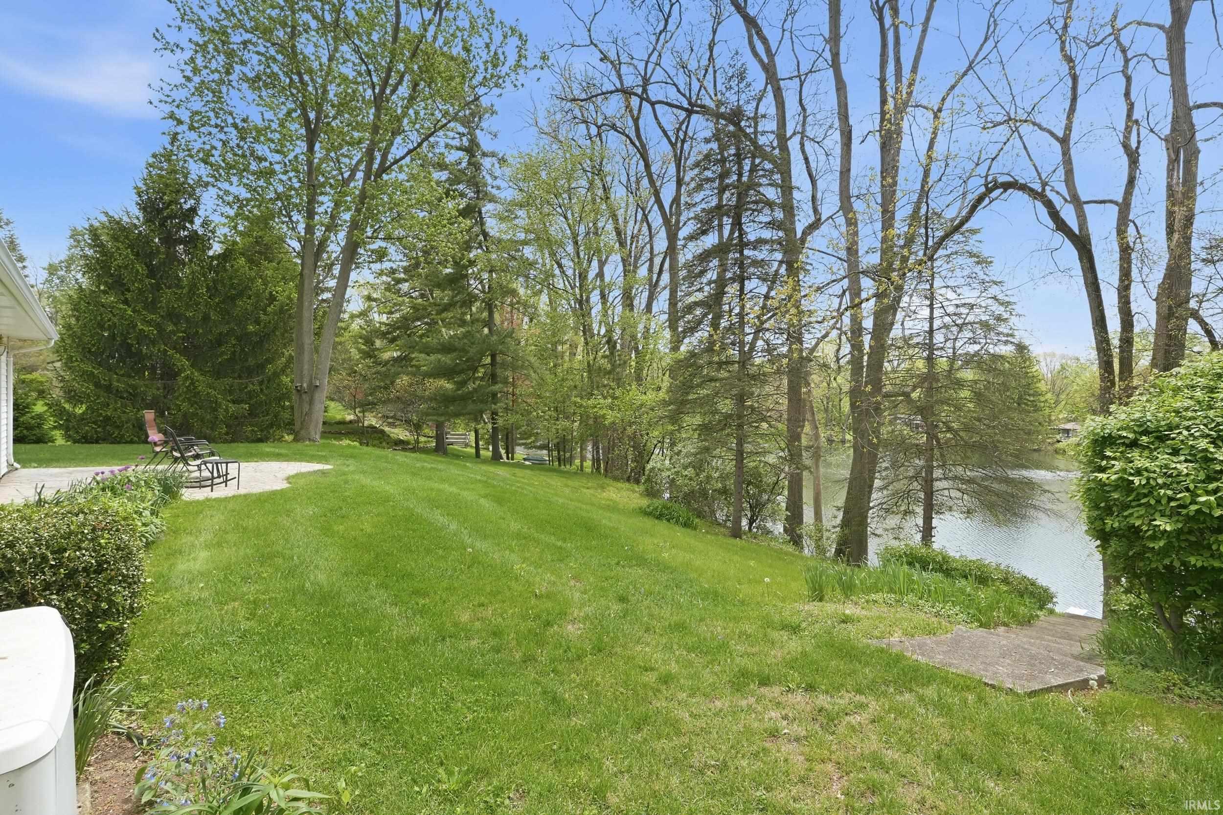 Expansive lawn area featuring a concrete patio, mature trees, and landscaping