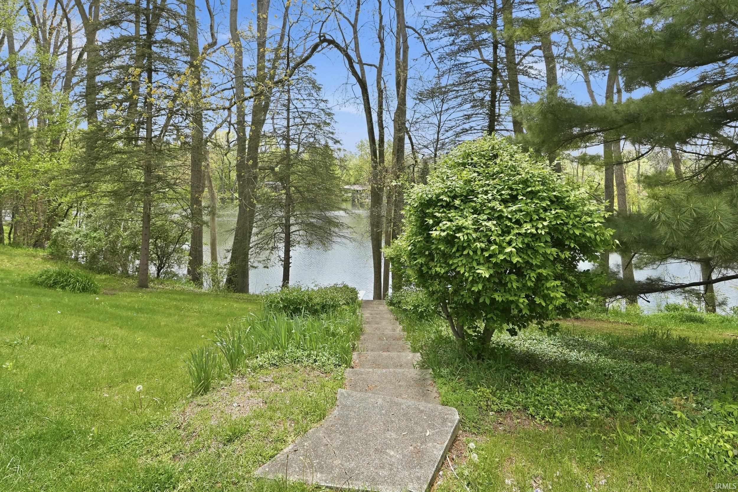 Lakeside property featuring a stone staircase descending to the water's edge, surrounded by mature trees and verdant landscaping