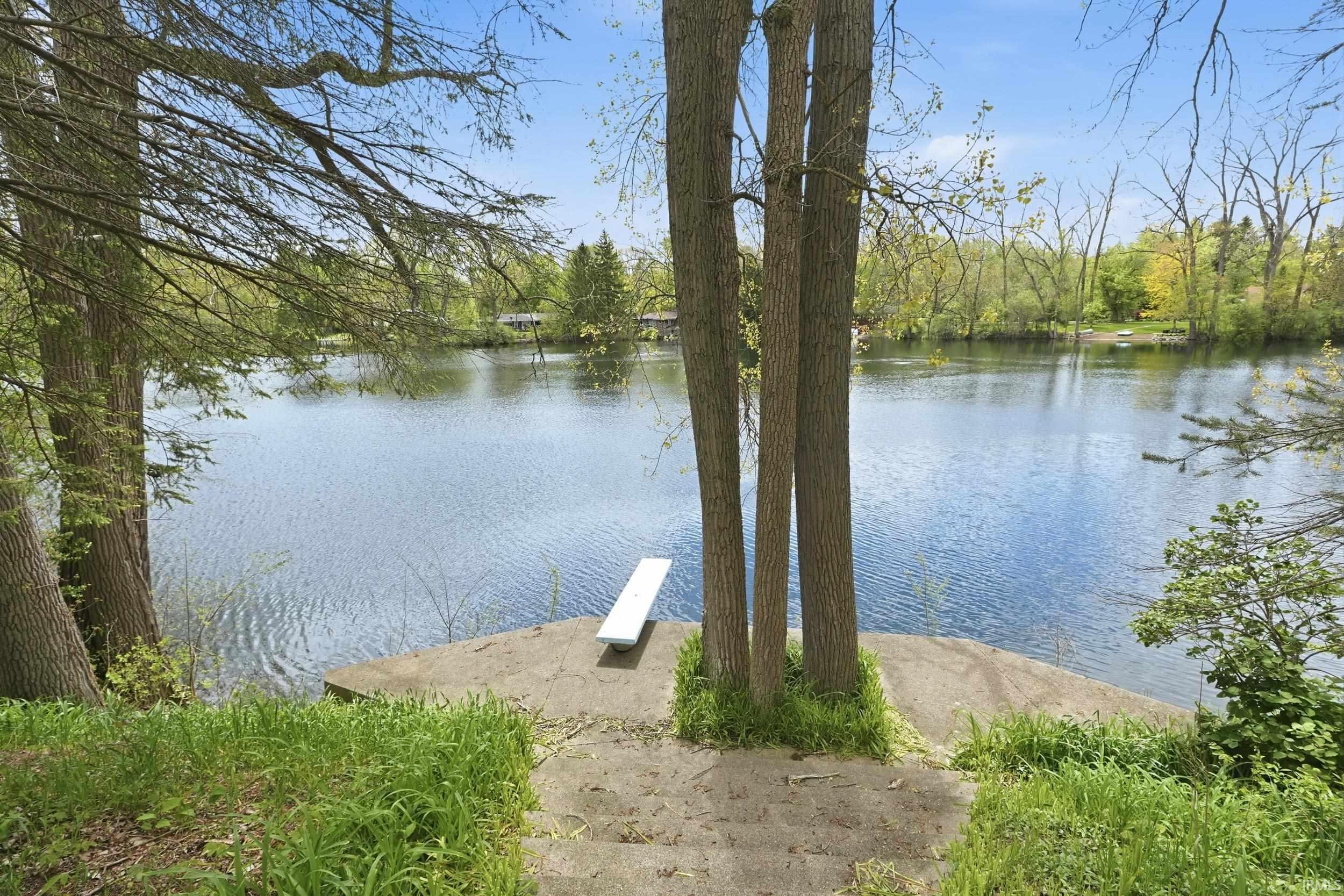 Waterfront property featuring a concrete platform with a diving board, natural landscaping, and mature trees