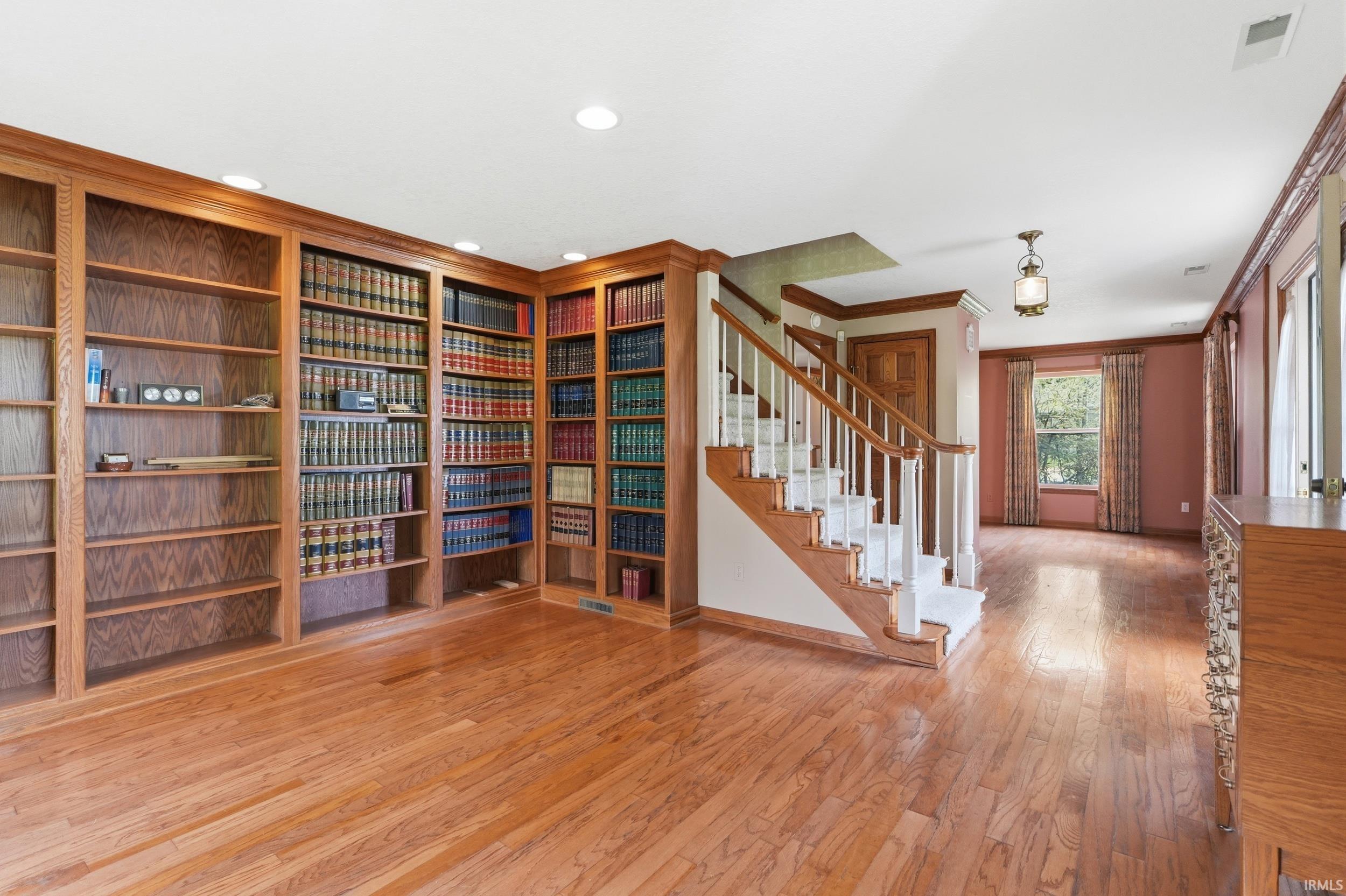 Expansive room featuring extensive built-in wood bookshelves, wood-finish flooring, and a staircase with white spindles and wood handrails