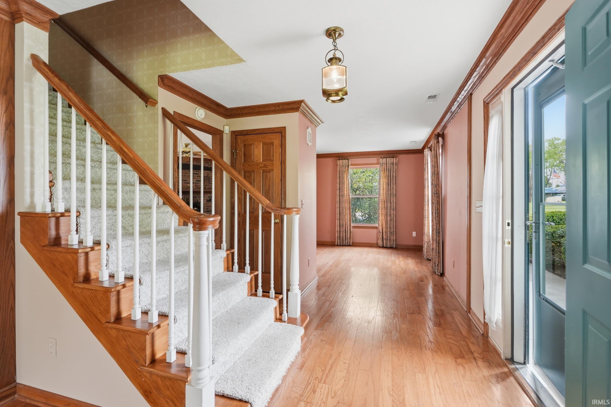 Entry foyer featuring wood-finish flooring, a carpeted staircase with wood handrails and white balusters, and a brass-tone hanging lantern fixture