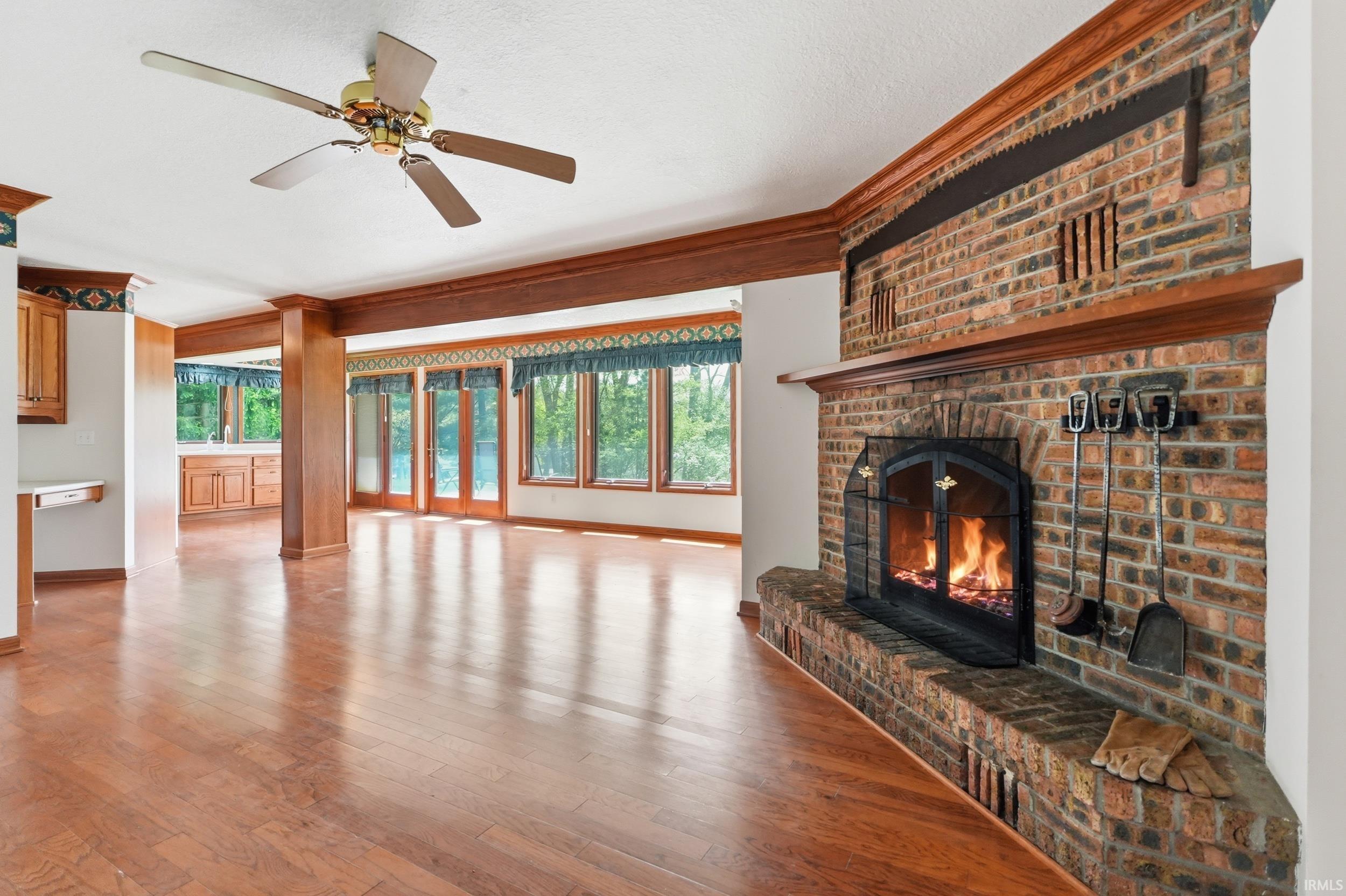 Brick fireplace with raised hearth, wood-finish flooring, exposed wood beams, and a ceiling fan